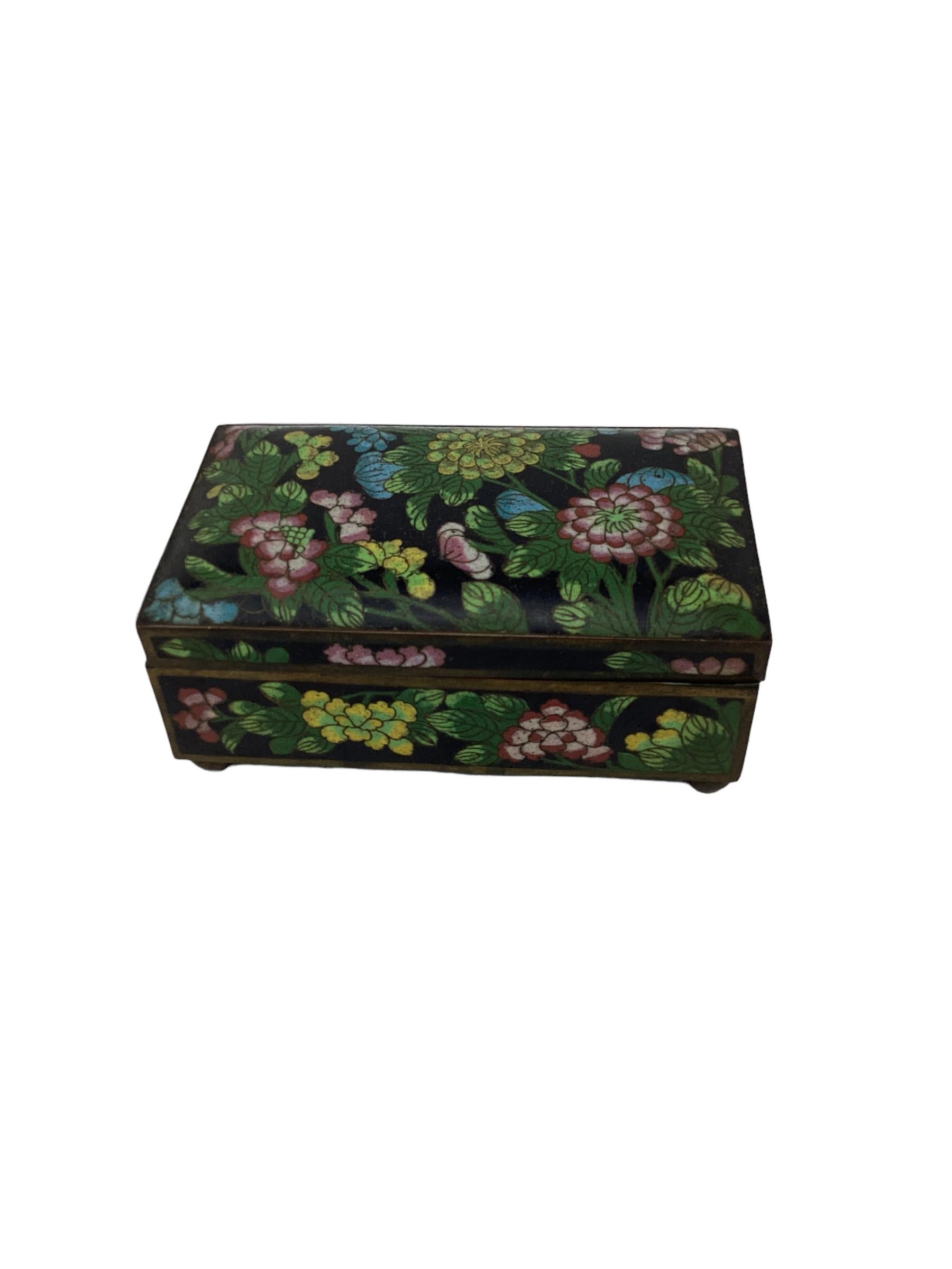 Lovely Chinese export cloisonné box made of brass and enameled with a beautiful floral pattern resting on ball feet. This decorative box was most likely a cigarette box or trinket box and would make a great desk accessory or cocktail table