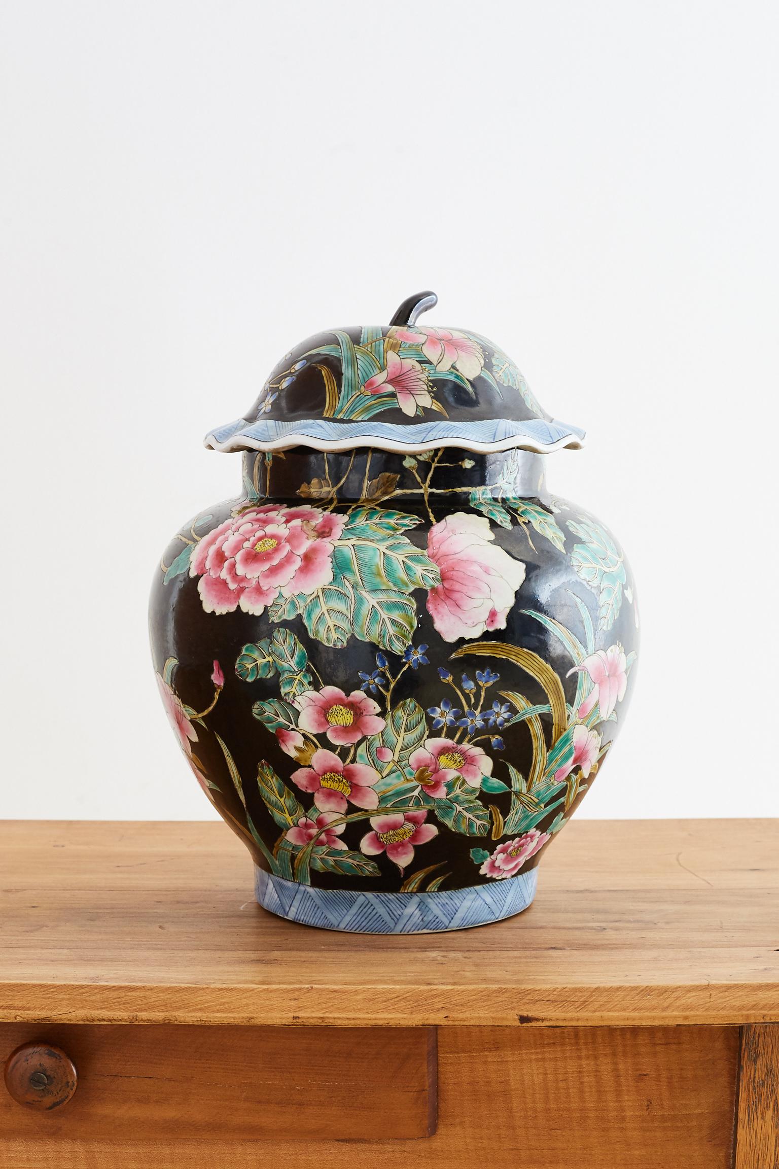 Colorful Chinese export famille noir porcelain ginger jar. Features an array of Famille Rose colors over a black ground with a matching lid. The lid and bottom of vase have a blue and white geometric pattern. The jar is decorated with floral and