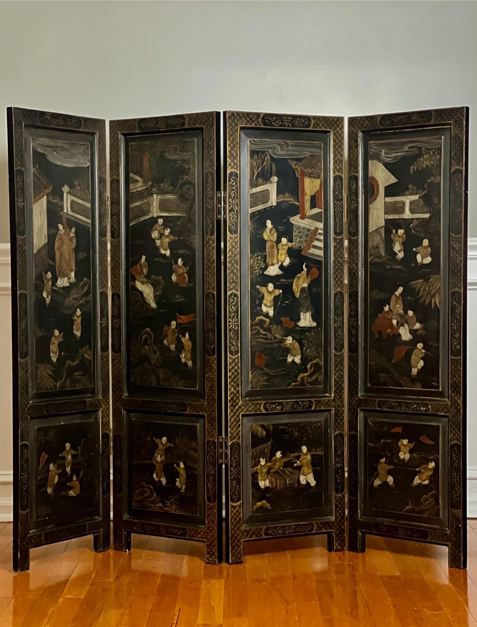 Chinese export smaller scale four-panel lacquered dressing screen room divider with hand-painted decoration on both sides.  

One side depicts a charming continuous pavilion scene with attendants watching over young boys enjoying various fun