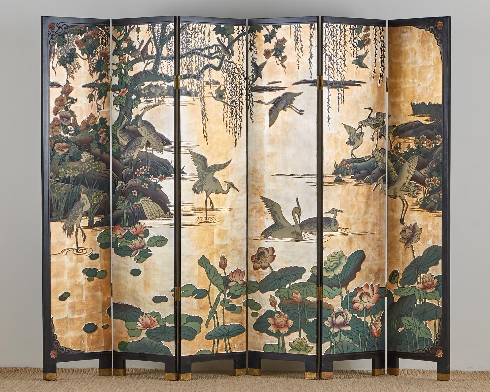 Stunning Chinese export six-panel Coromandel screen featuring a water landscape with cranes on a dramatic gilt background. The beautiful carved scene runs the entire length of each panel and is decorated with lotus, lily pads, willow, and flowers.