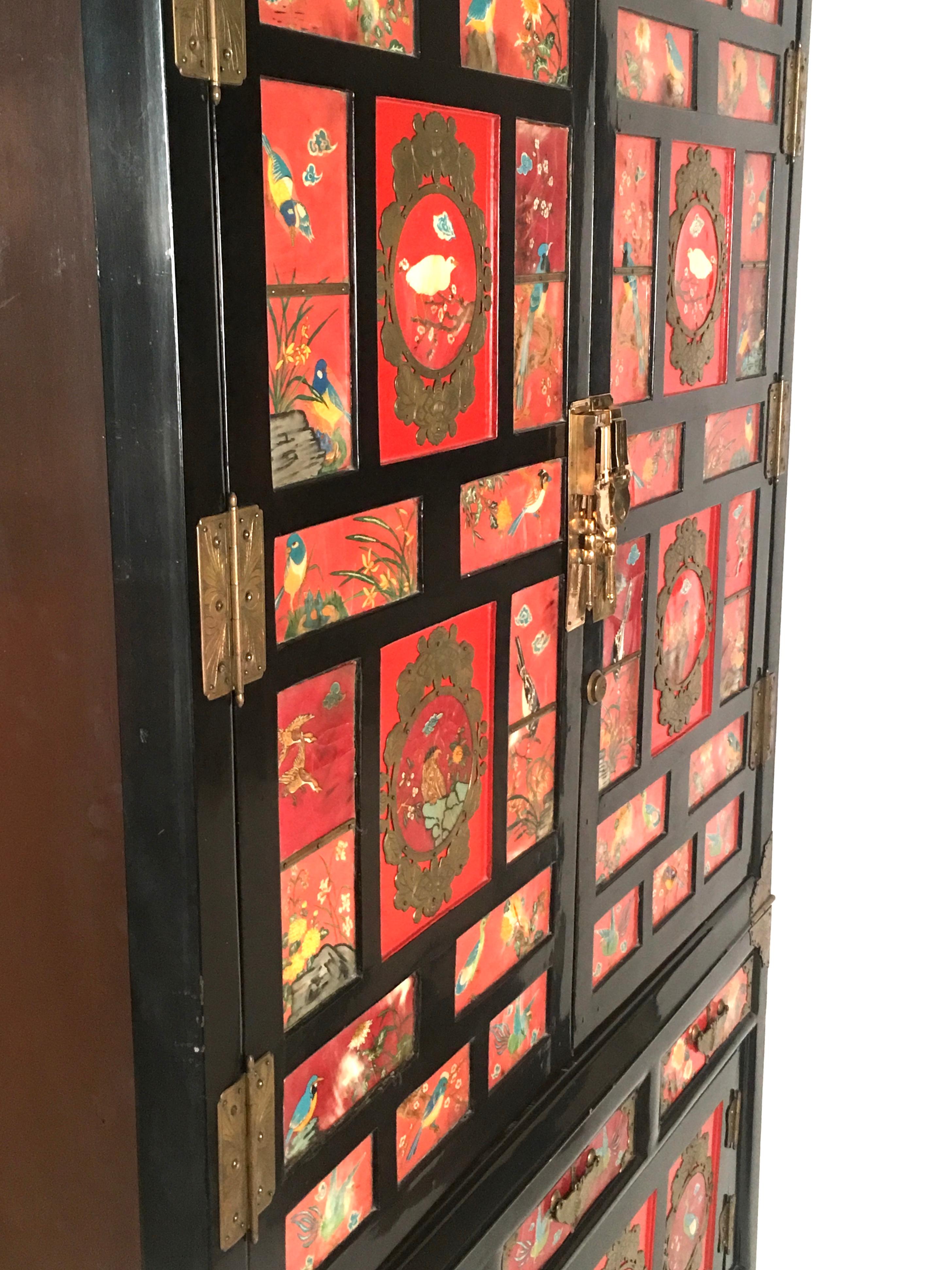A striking Chinese export black lacquered cabinet of rectangular form, the front decorated overall with inset panels of hand-painted colorful birds on a red field, with brass mounts, shaped and engraved in butterfly and moth forms, comprising two