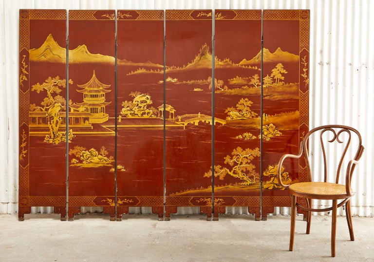 Remarkable Chinese export six-panel coromandel screen featuring a crimson red ground and parcel gilt decorated landscape scene. The idyllic painting is crafted in a moriage style (raised pigments) with intricate details and a geometric border. The