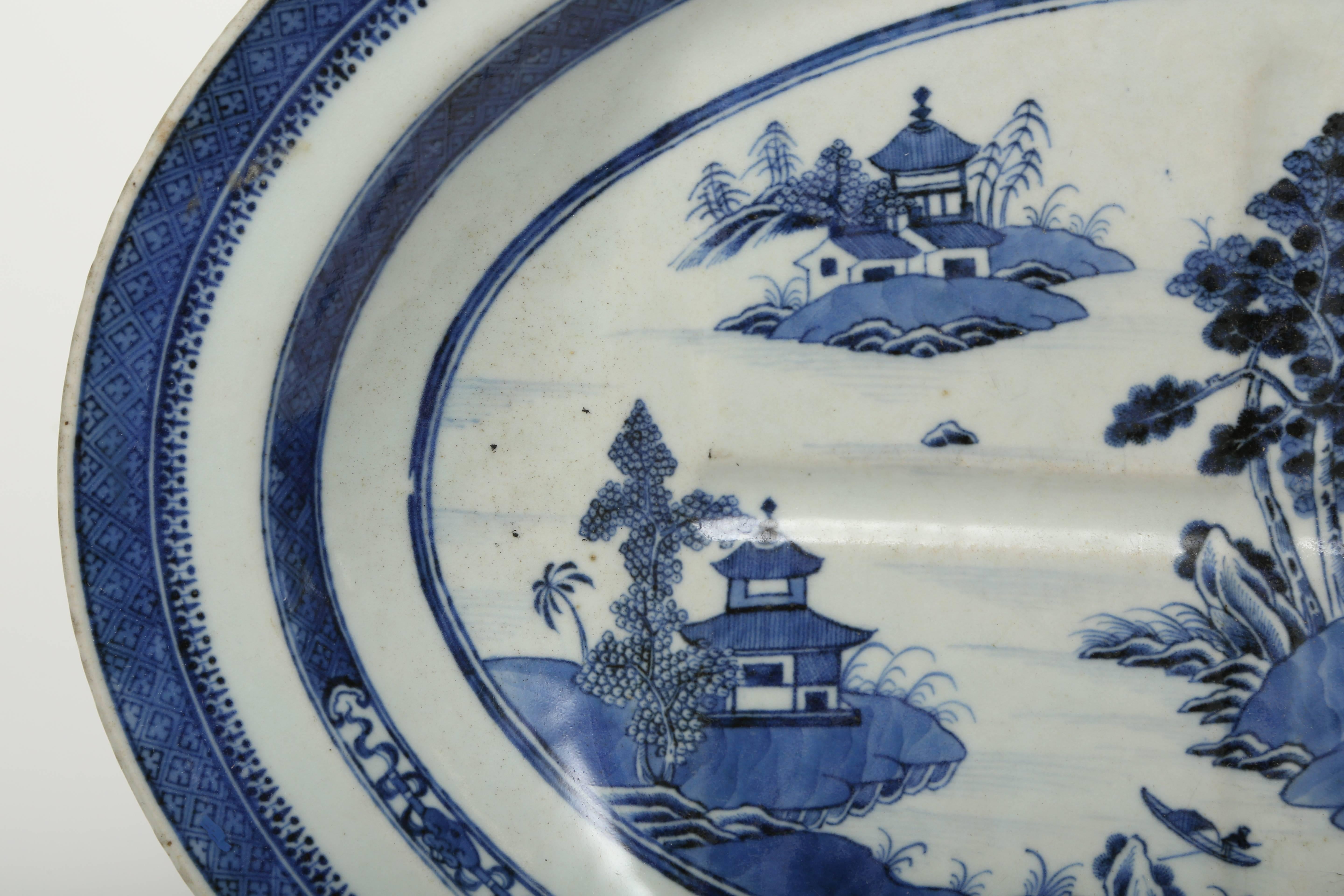 Plat d'exportation chinois à motif de puits et d'arbres de Nankin. Cette porcelaine de forme ovoïde est décorée d'un bleu sous glaçure.  La double bordure est caractéristique du motif de Nankin.  Ce plateau est d'une couleur bleue vive et en très