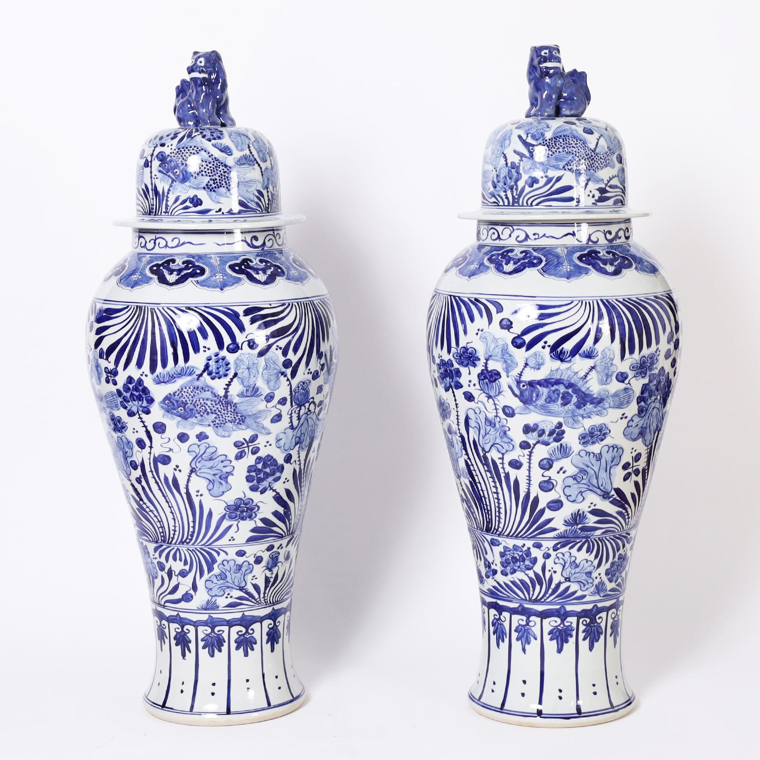Striking pair of Chinese blue and white porcelain urns with cat lid handles and ambitiously hand decorated with aquatic fauna and flora having a rare touch of whimsy. 
