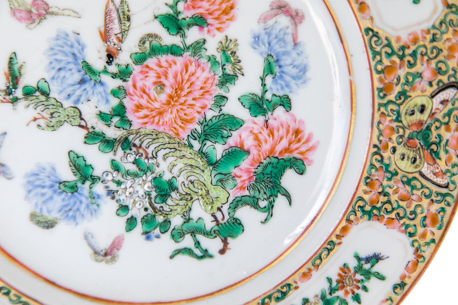 Chinese Export plate, with the center panel of the plate painted with pink and blue chrysanthemums, butterflies, and a grasshopper. The border has four panels depicting fruit and flowers as well as a brocaded floral pattern with butterflies on a