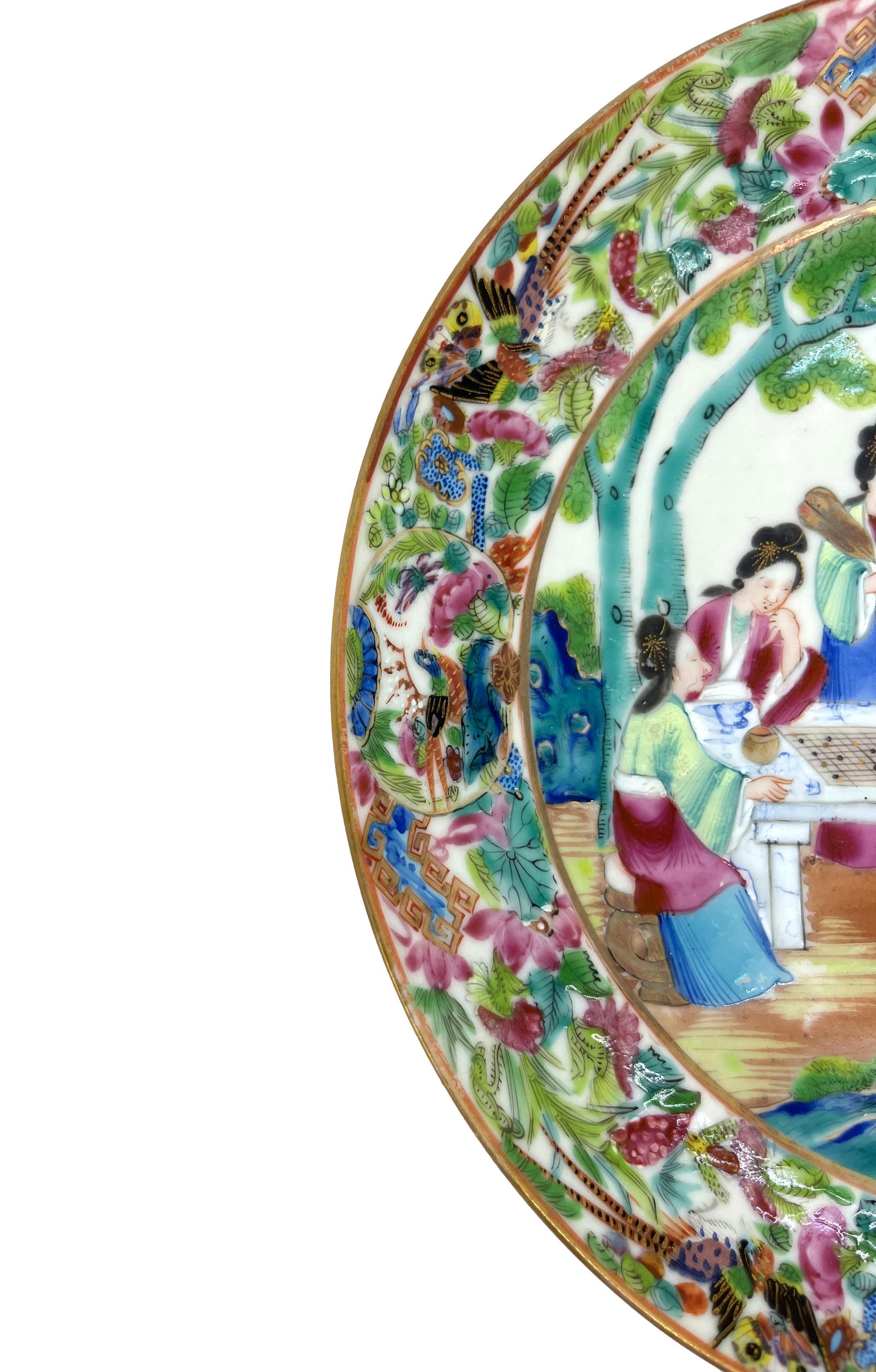 Chinese Export Porcelain Canton Famille Rose plate, ca. 1820. The round plate with a central design depicting a theatre pavilion Imperial Court scene with figures at a Wei Qi board, with hyper-vivid enamels and fine gilt accents, with multi-layered