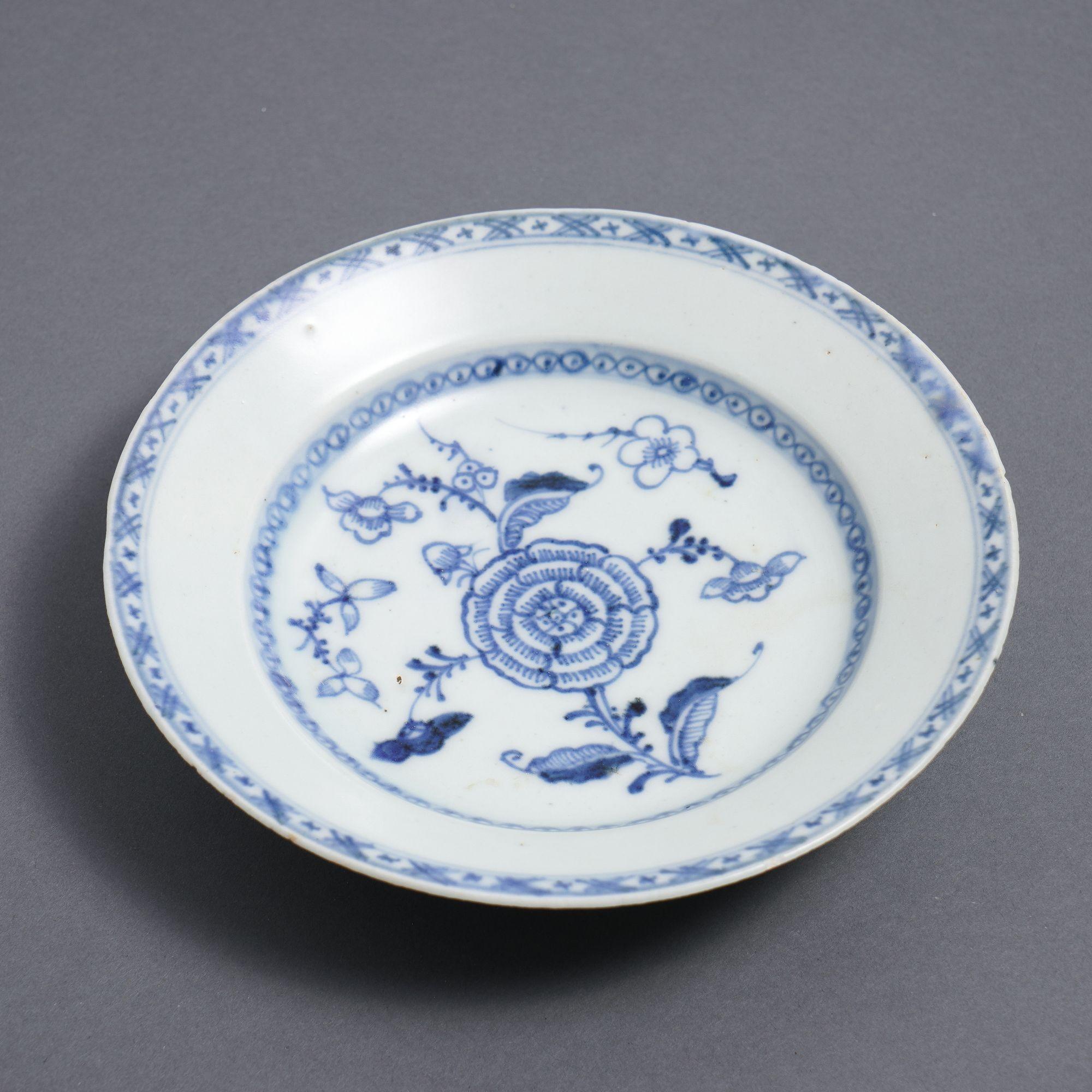 Chinese export porcelain rim soup decorated in cobalt underglaze blue. The pattern centers on a blooming flower surrounded by scattered prunus boughs within the border of the dished center. The flat canted rim is bordered with cobalt cross hatching