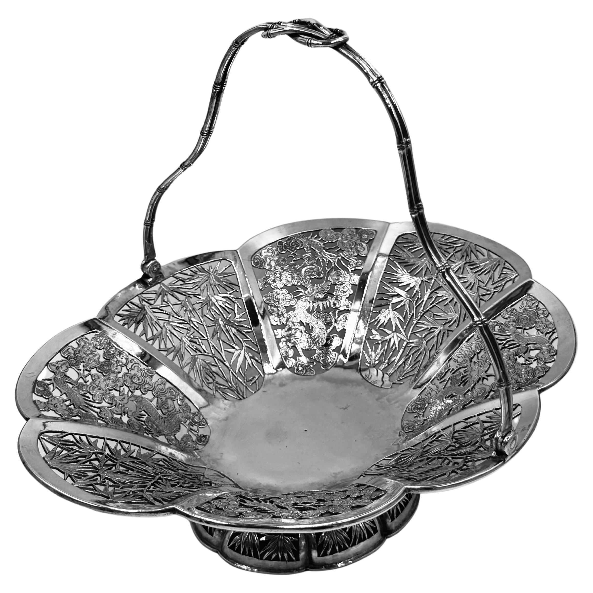 Cesta china de plata de exportación, hacia 1895, de forma ovalada. El plato tiene ocho paneles alternos de bambú grabado y perforado, y dragones voladores entre nubes auspiciosas. La base presenta un faldón de bambú perforado, y el mango está