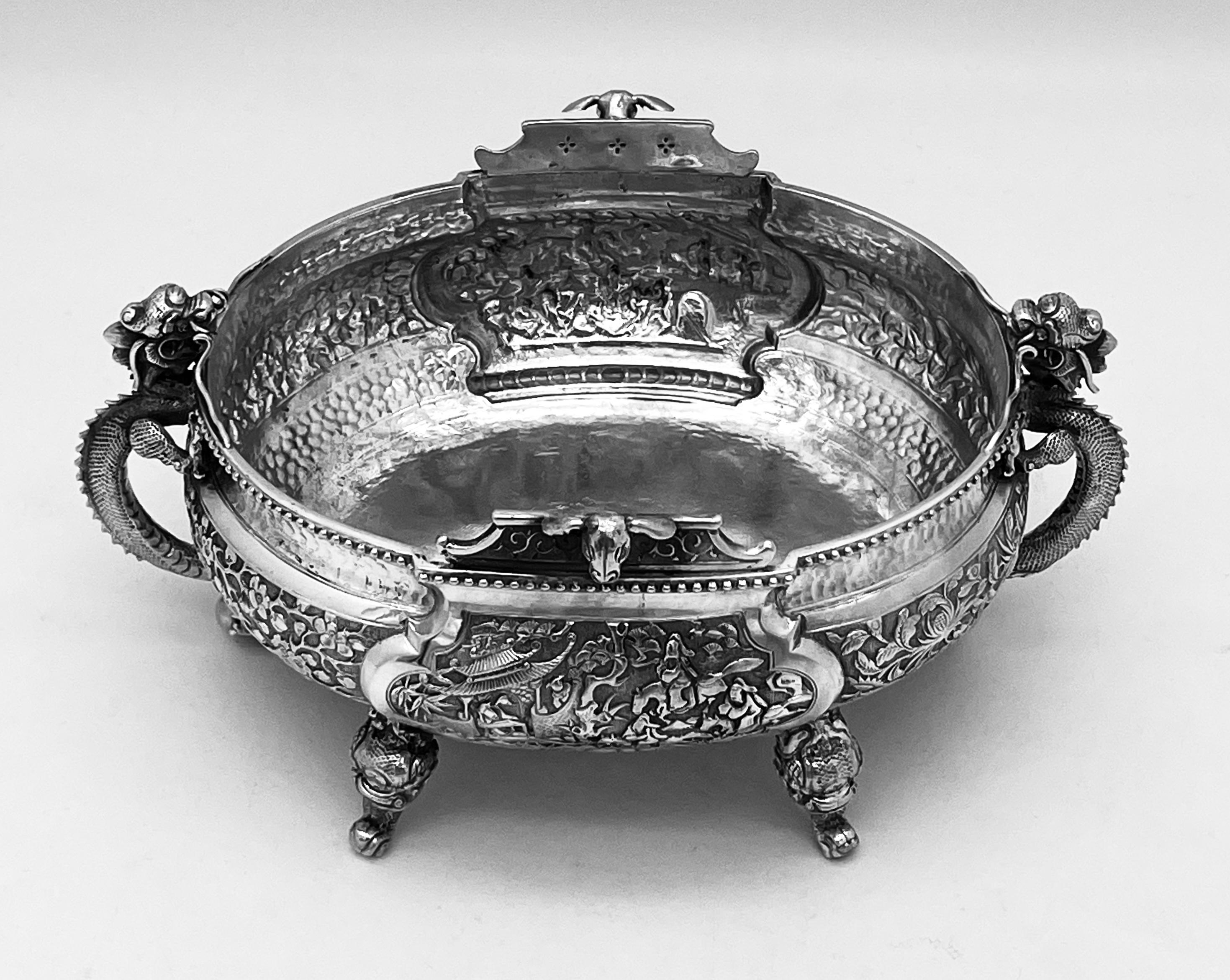 A Chinese export silver oval bowl or jardiniere, made by Tu Mao Xing, '涂茂興‘, circa 1890. There are two dragon handles, and four dragon feet. There is a beaded rim and two animal heads, possibly sheep, looking out. The main panels depict the story of