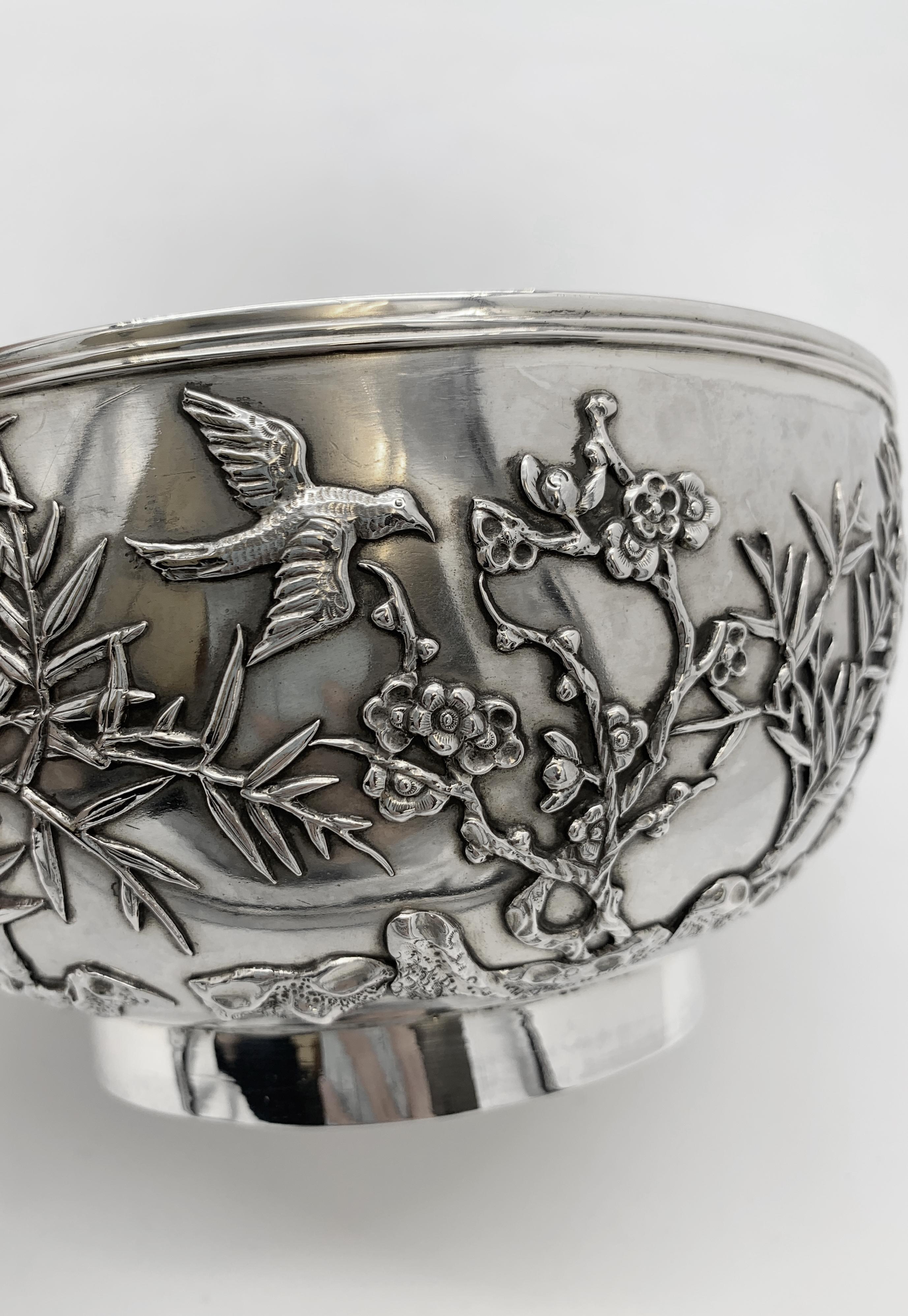 Chinese Export Silver Bowl, circa 1890, round and sitting on a plain collet foot. The bowl is applied with bamboo and prunus emerging from rocks, and also two birds in flight. The bowl is marked WH for the retailer Wang Hing; a 90 which is sometimes