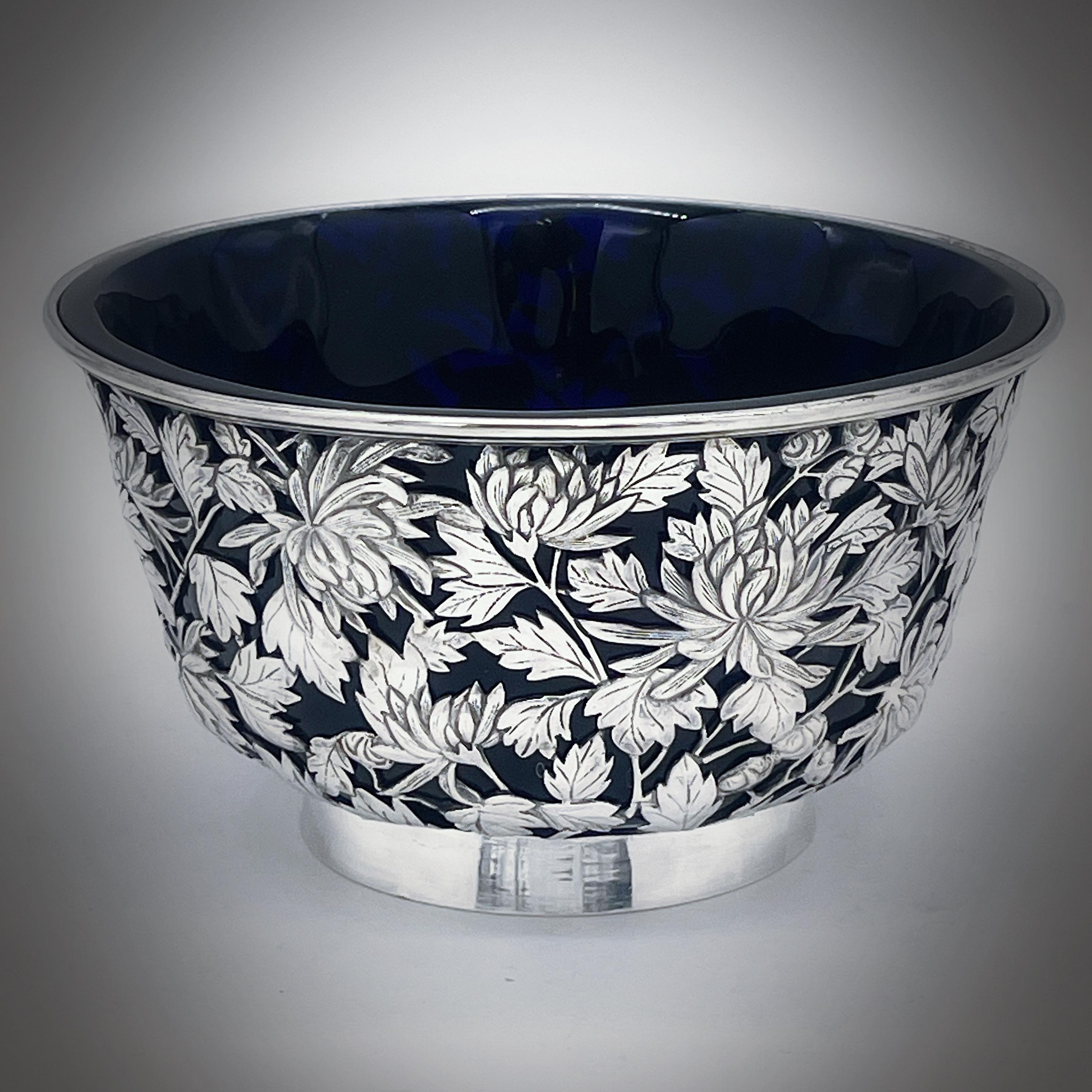 Un bol en argent d'exportation chinois vers 1890, avec une doublure en verre bleu plus tardive. La coupe est percée et présente un décor de chrysanthèmes merveilleusement détaillé. Elle repose sur un pied à collet uni. La marque du détaillant est KC