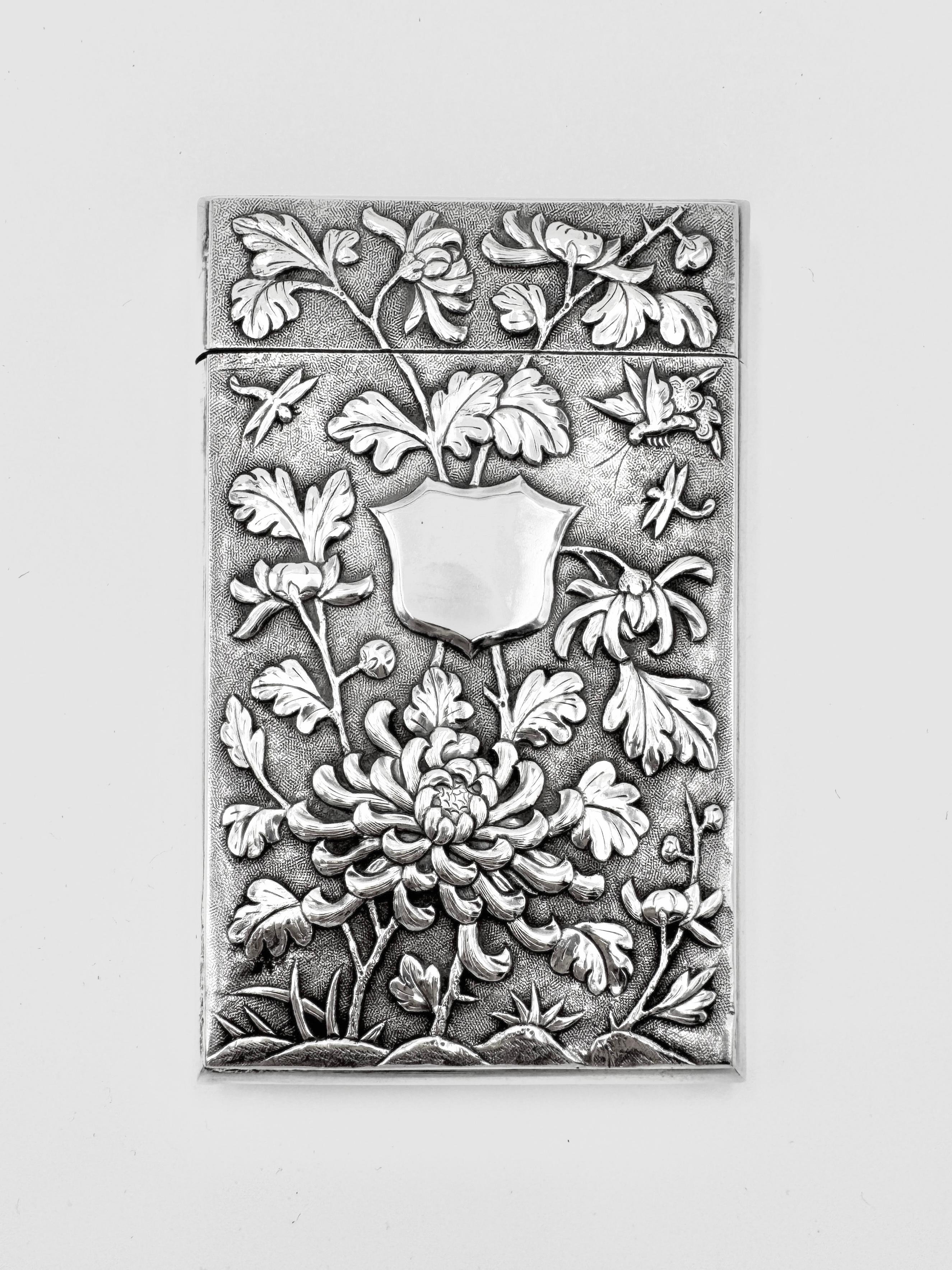 Chinese Export Card Case, circa 1885, embossed and chased with figural scenes on one side, and crythusanmum, a butterfly and two flydragons surrounding a single vacant shield-shaped cartouche on the other side, both set against a matte background.