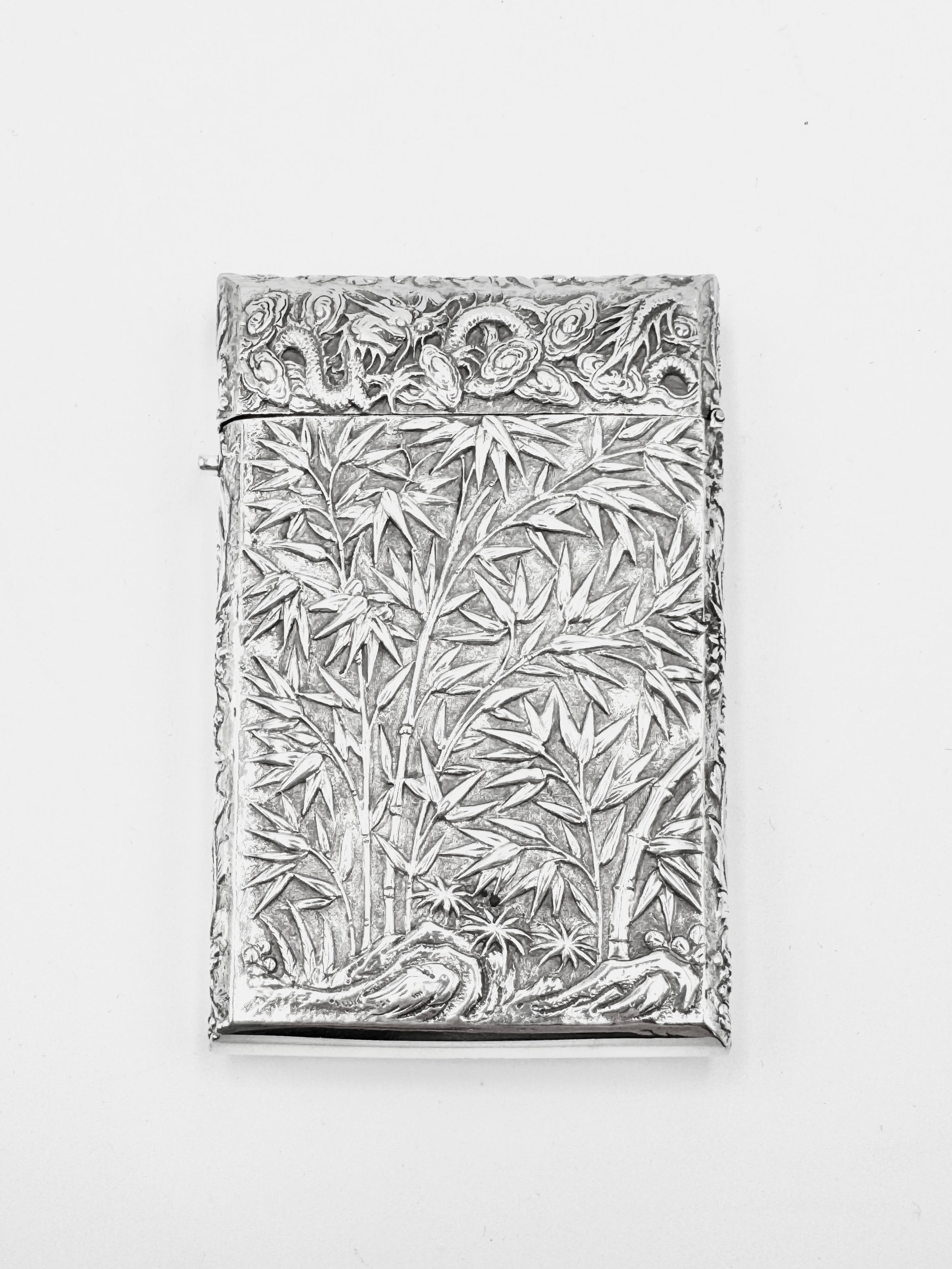 Chinese Export Card Case, circa 1885, embossed and chased with figural scenes on one side with a single vacant shield-shaped cartouche, and bamboo on the other side, both set against a matte background. The card case has a round button on the side