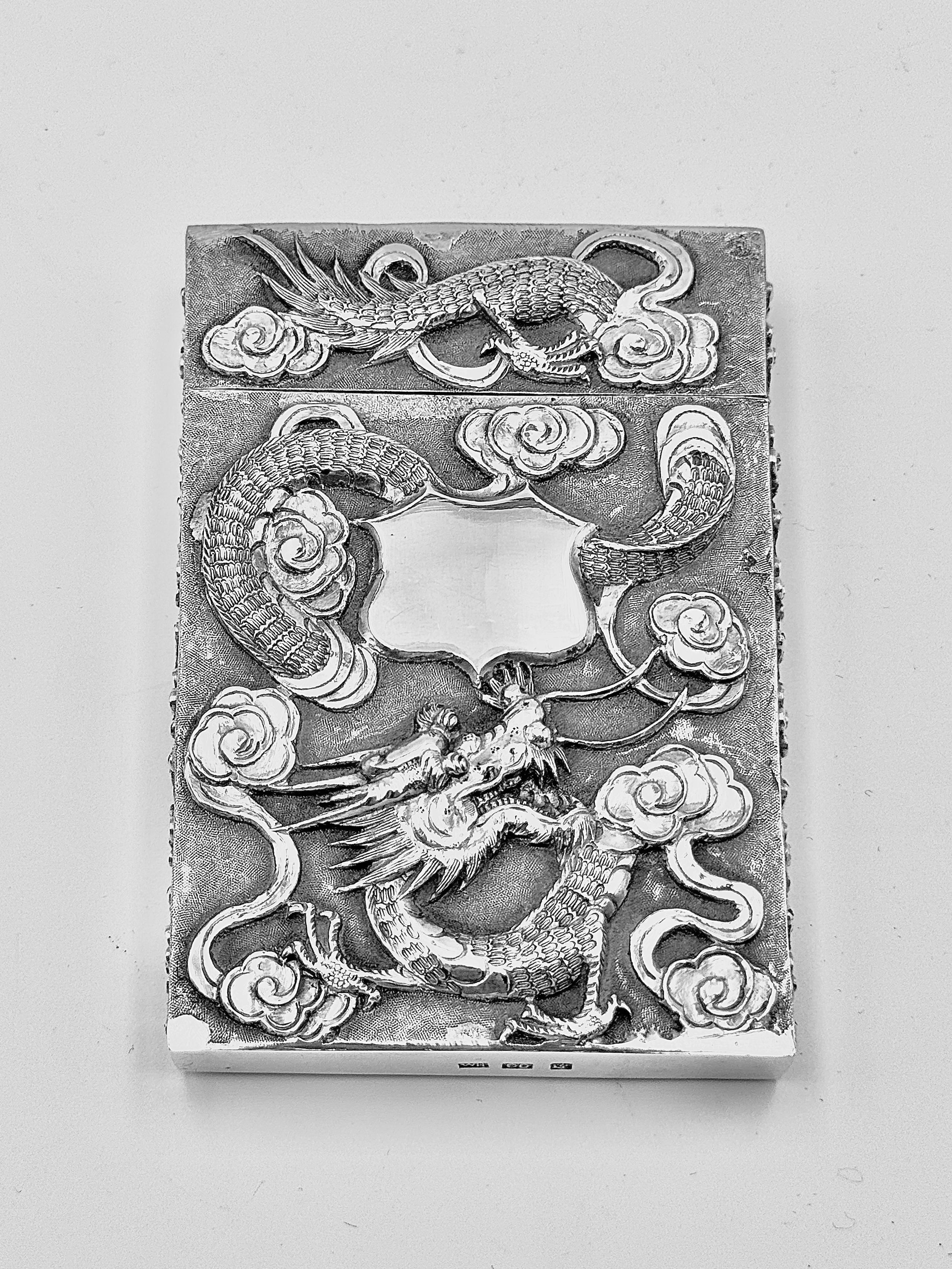 Chinese Export Silver Card Case, circa 1890, embossed and chased with a dragon among clouds on one side, featuring a single vacant shield-shaped cartouche; the reverse decorated with prunus blossoms and branches, both sides set against a matte