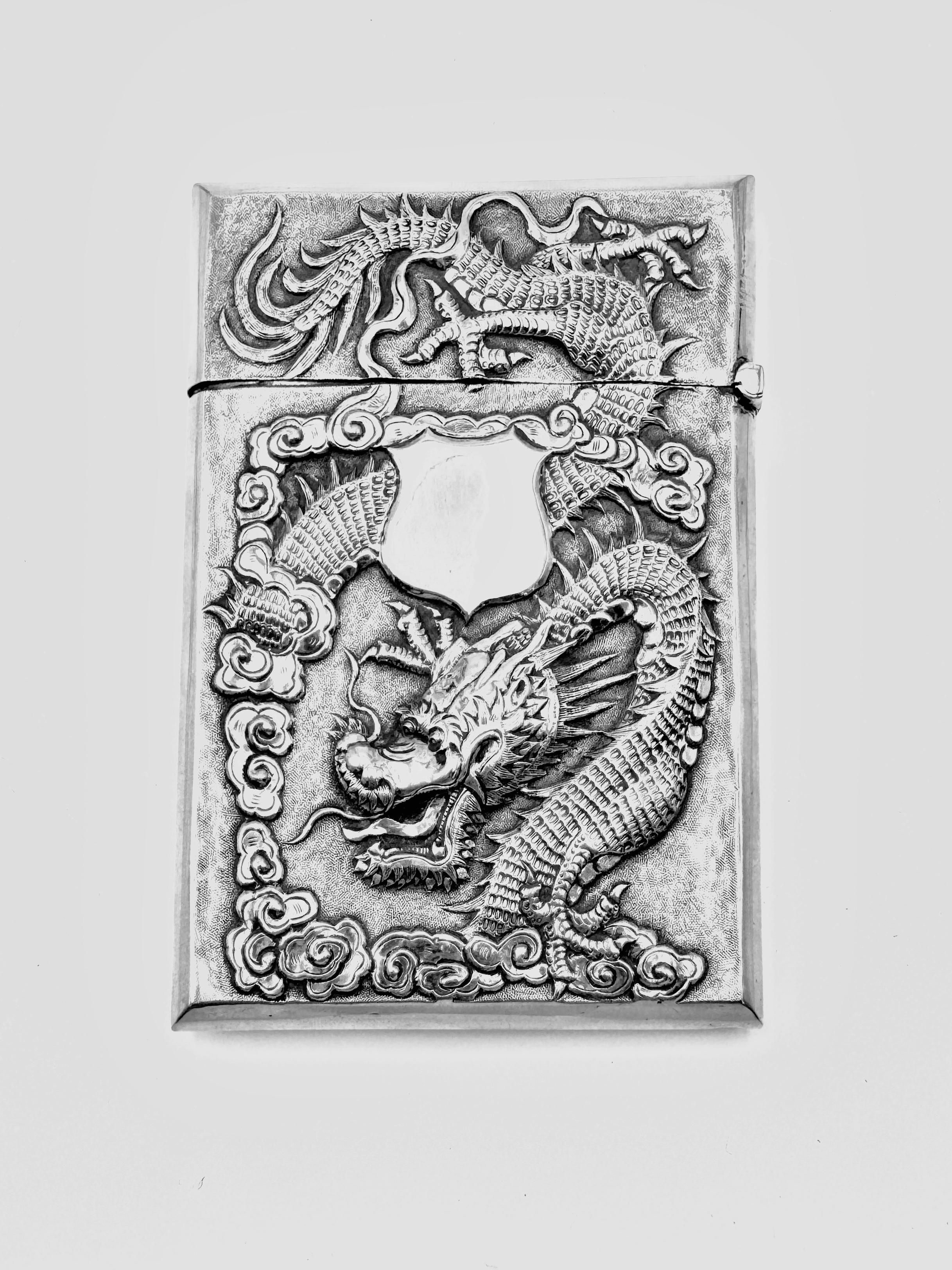 Chinese Export Silver Card Case, circa 1900, embossed and chased with a dragon amidst clouds on one side, and with a vacant shield-shaped cartouche. The reverse side features chrysanthemum blossoms. The card case has a hinged lid at the top. Marked