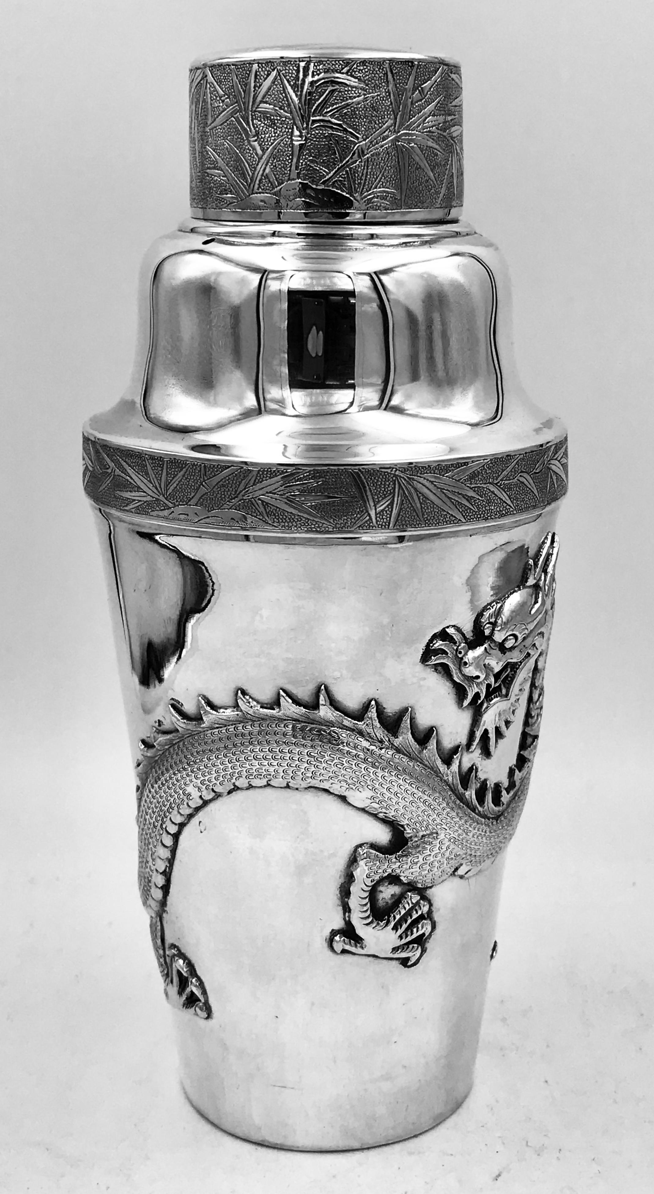 A Chinese silver cocktail Shaker of plain form with an applied dragon swirling around the body. The cover and the border have a band of bamboo engraving.