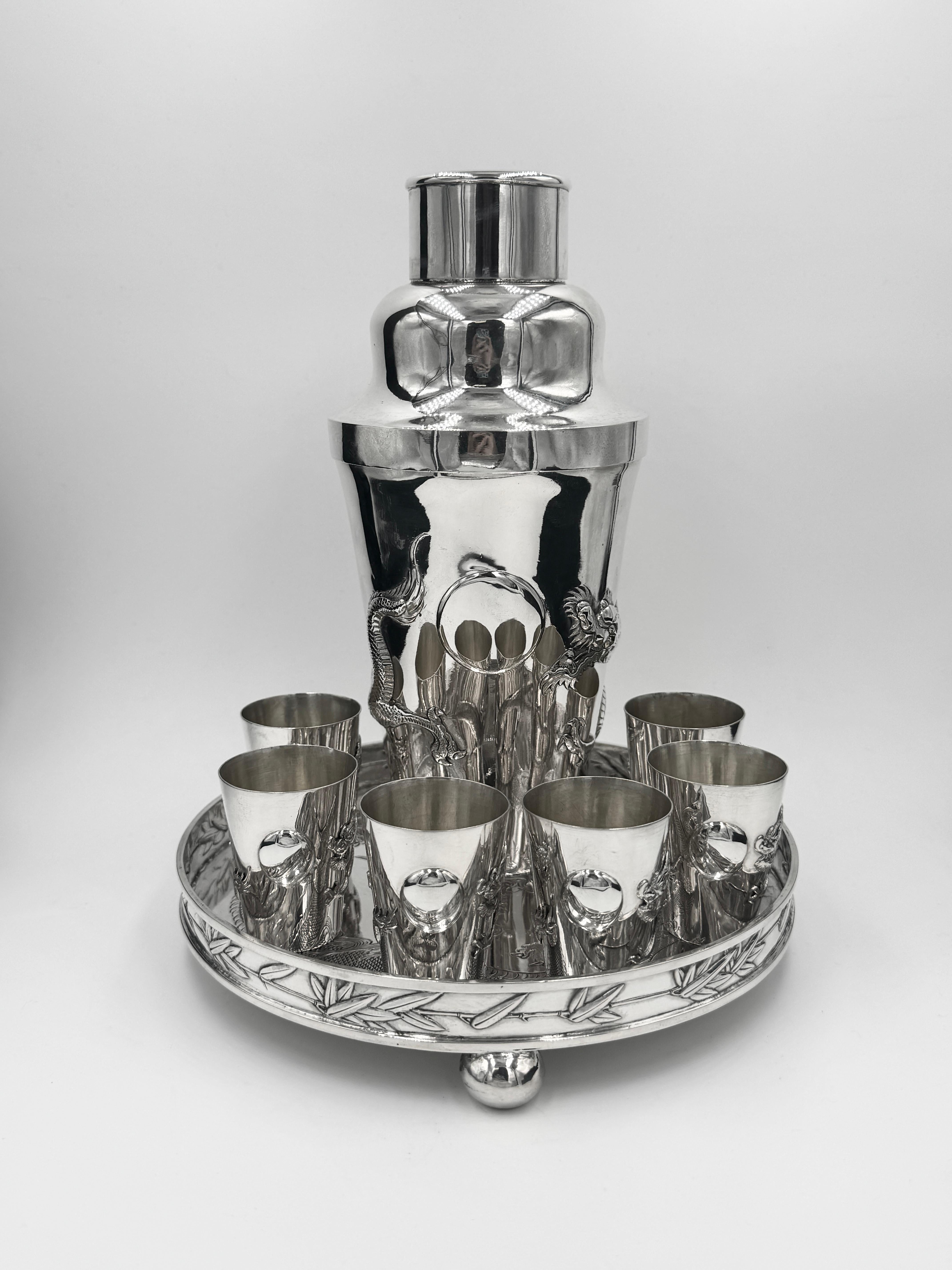 Shaker da cocktail in argento da esportazione cinese, vassoio e 6 bicchieri, Hong Kong, circa 1920. Lo shaker da cocktail e i bicchieri da shot hanno una decorazione a drago applicata e un cartiglio rotondo libero. Il vassoio rotondo, che poggia su