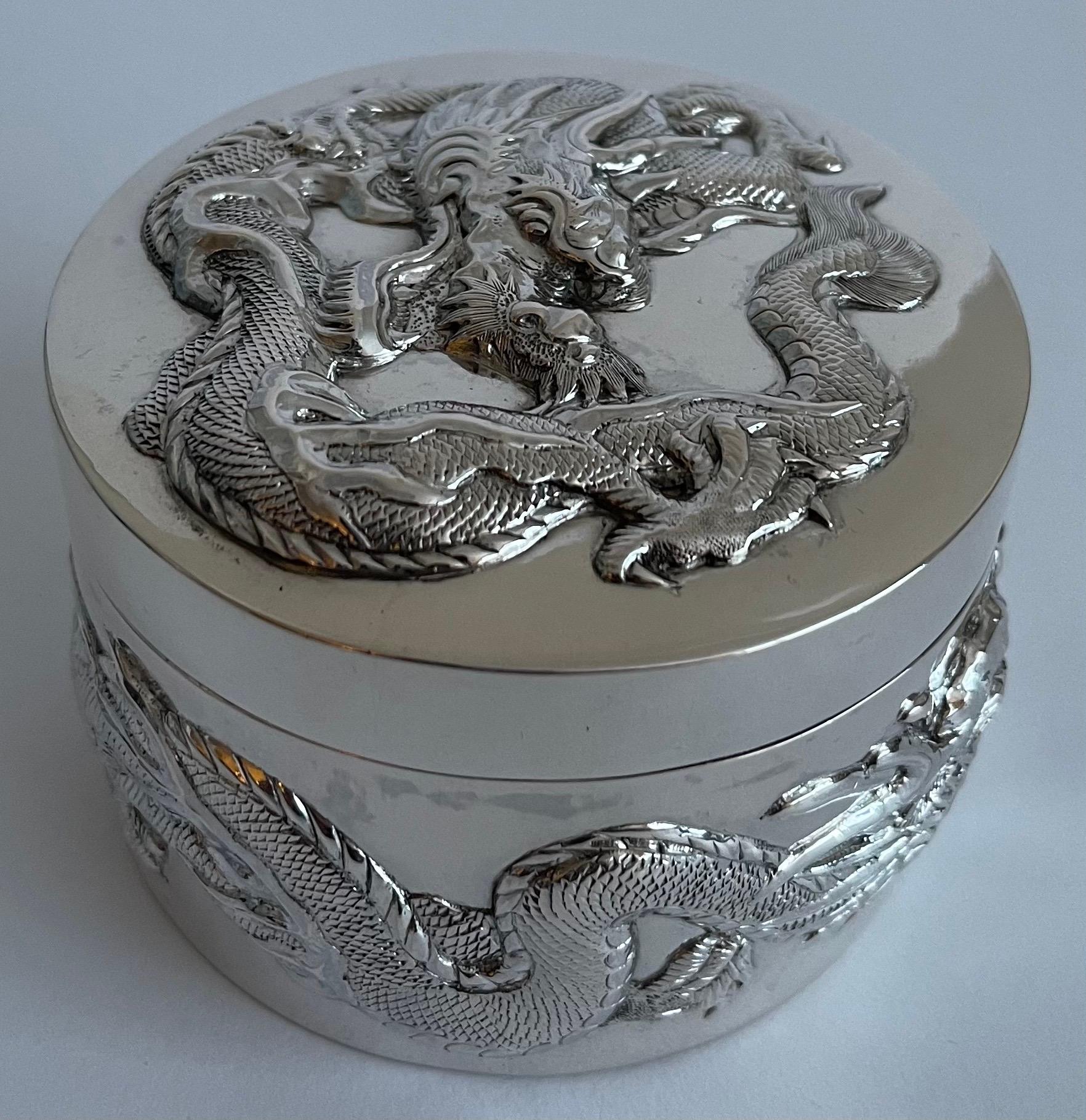 Chinese export silver cylindrical box. Singular writhing repoussè dragon with flames motif wraps around the base. 
The lid of the box features another singular dragon in a whirling position to compliment the circular design. 
Makers mark on the