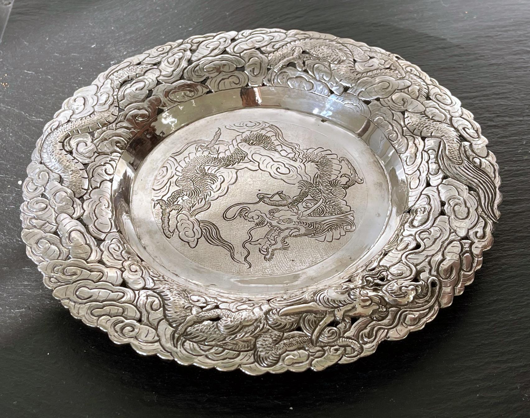 An elaborately decorated silver serving dish or butler's tray, likely dated to the turn of the 20th century, made in China for the export market. The round tray has a solid center in contrast with a pierced outer band of repoussé design that depicts