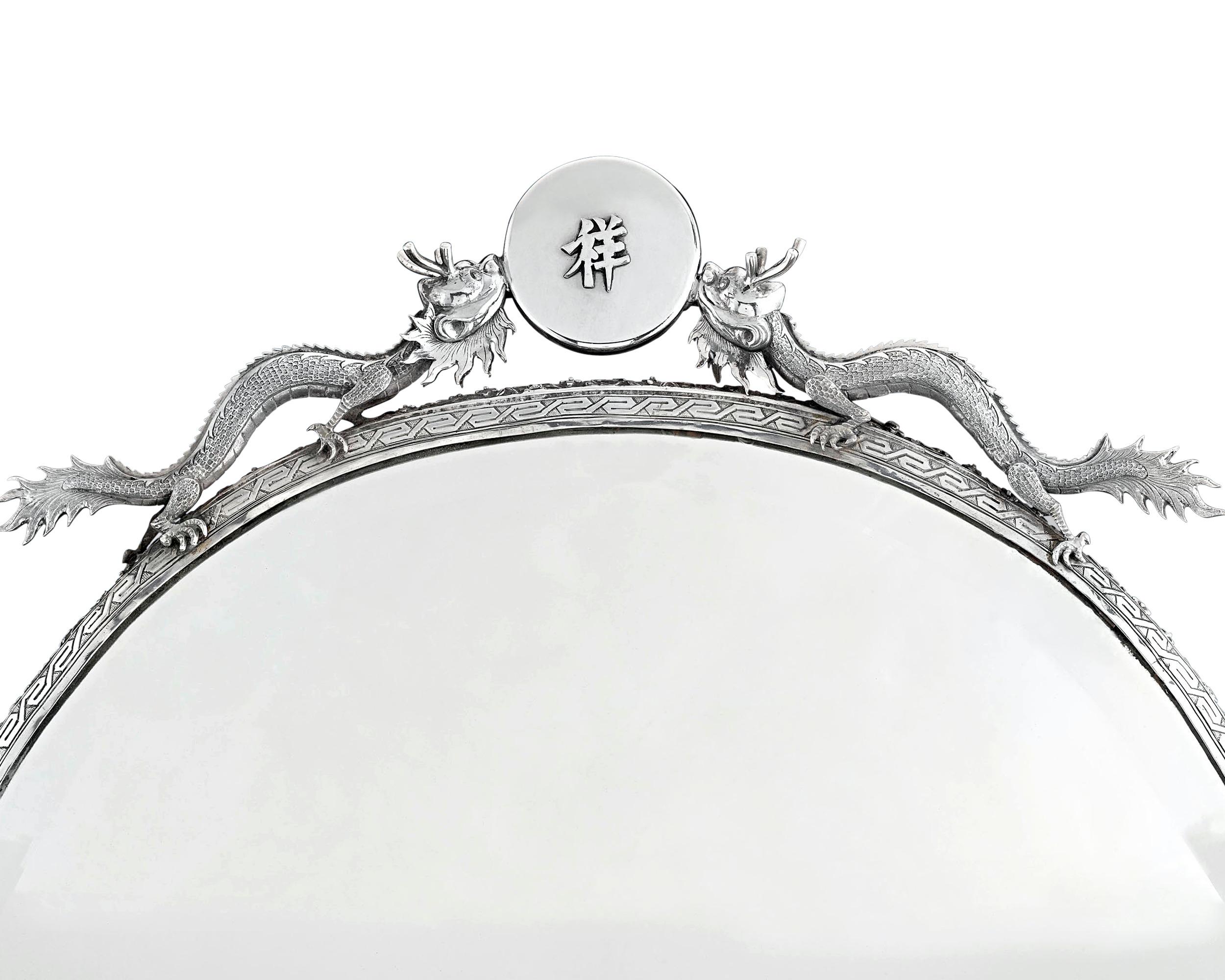 Ce miroir exquis en argent exporté de Chine est une œuvre d'une beauté exotique. D'une forme élégante et d'une taille monumentale, ce miroir est maintenu dans un cadre en argent d'un art extraordinaire, avec une bordure florale ciselée et gravée, et