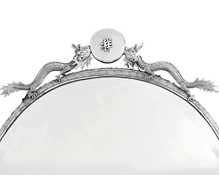 This exquisite Chinese export silver mirror is a work of exotic beauty. Elegantly shaped and monumental in size, this looking glass is held within a silver frame of extraordinary artistry, boasting a chased and engraved floral boarder and guarded by