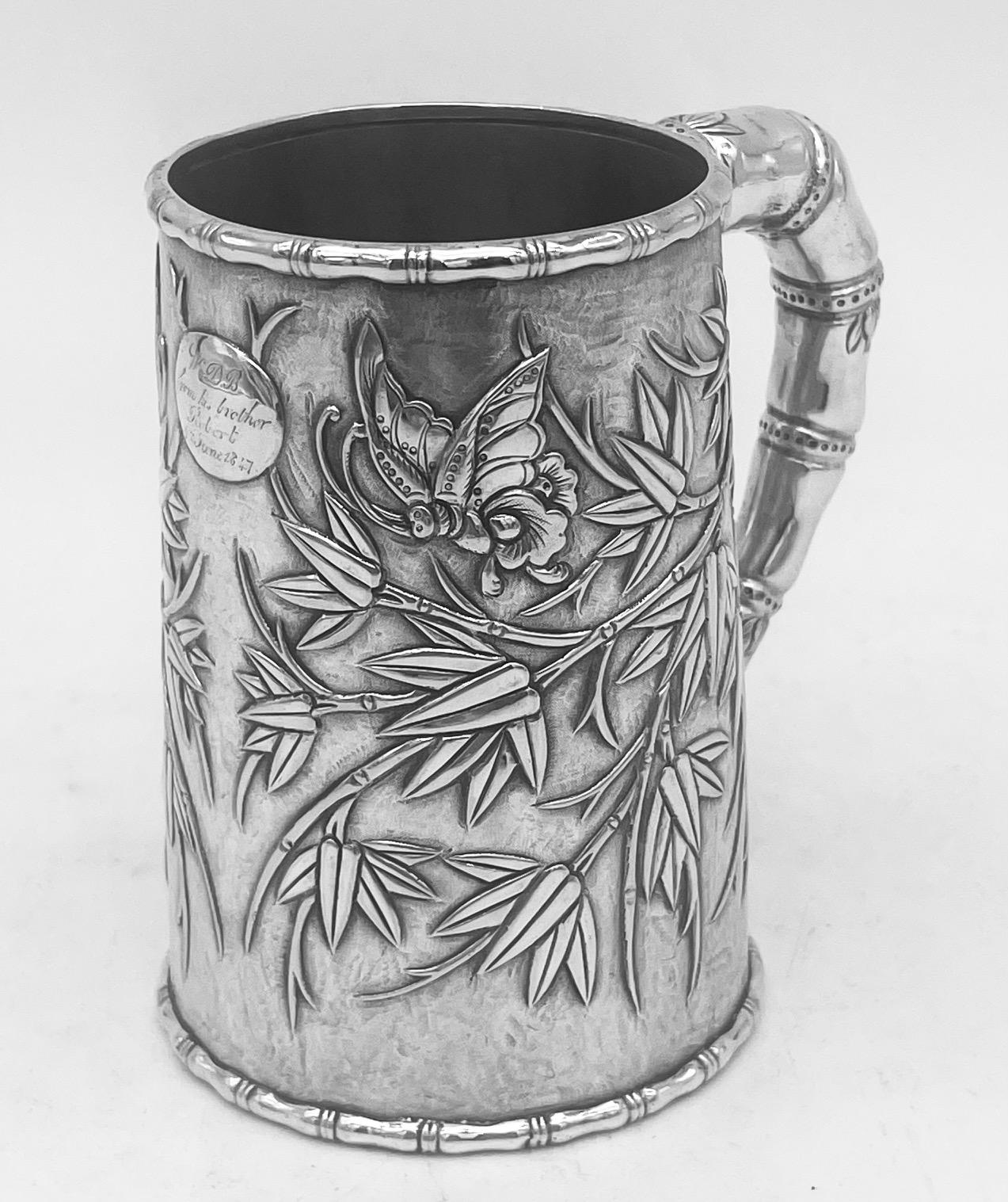 An interesting and delightful Chinese export silver mug, of double-skin construction and decorated with bamboo leaves against a matte background. The small oval cartouche, which is flanked by two splendid looking winged insects, is engraved with an