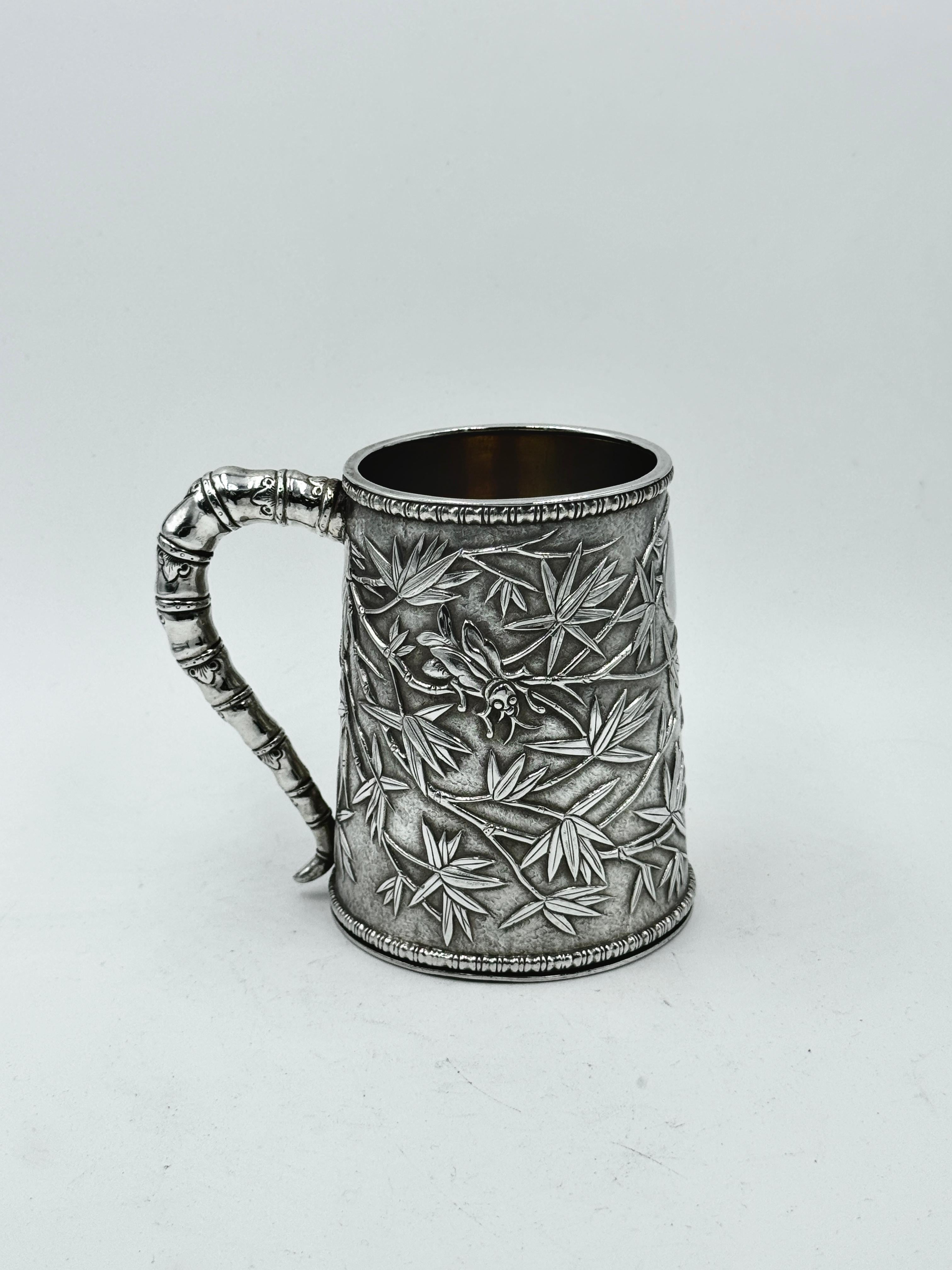 Taza china de plata de exportación de hacia 1850, de doble piel y decorada con hojas de bambú y dos grillos sobre fondo mate, asa de bambú simulada y cartela oval vacía. La marca del fabricante es HCH junto con pseudomarcas, que se utilizaban a