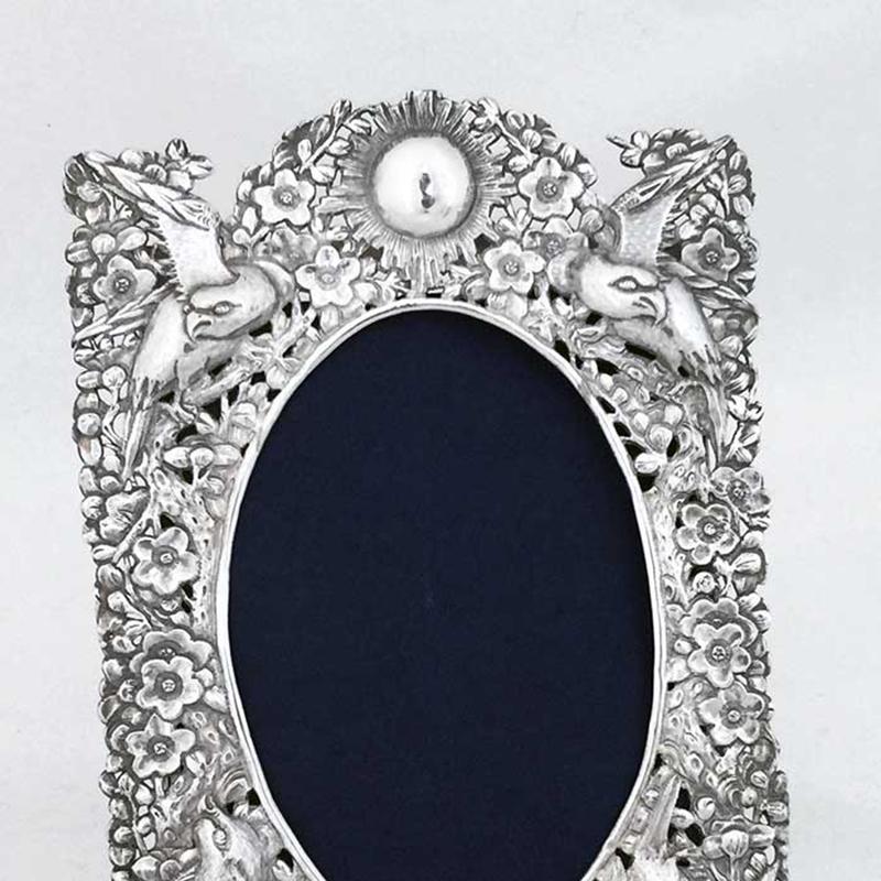 A finely worked Chinese Export silver photograph frame.

The border around the oval reserve of this rectangular frame is closely repousse and pierced worked with the plum blossom motif. Birds are worked within the blossoms. There is a round