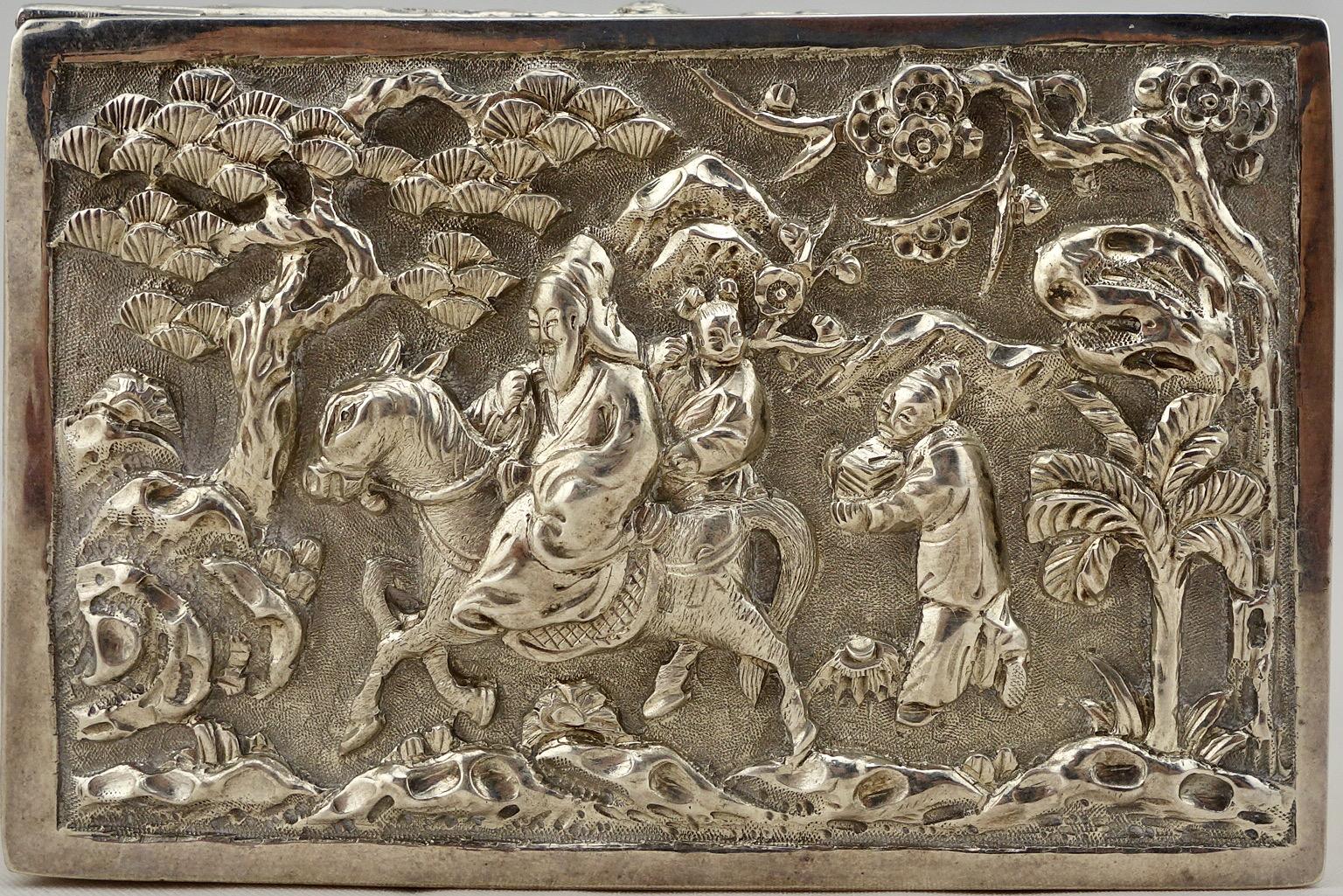 Scatola scenica cinese in argento repousse, raffigurante una scena tradizionale di un mandarino che cavalca il suo cavallo sul coperchio. I lati sono decorati con motivi vegetali stilizzati. Marchio 