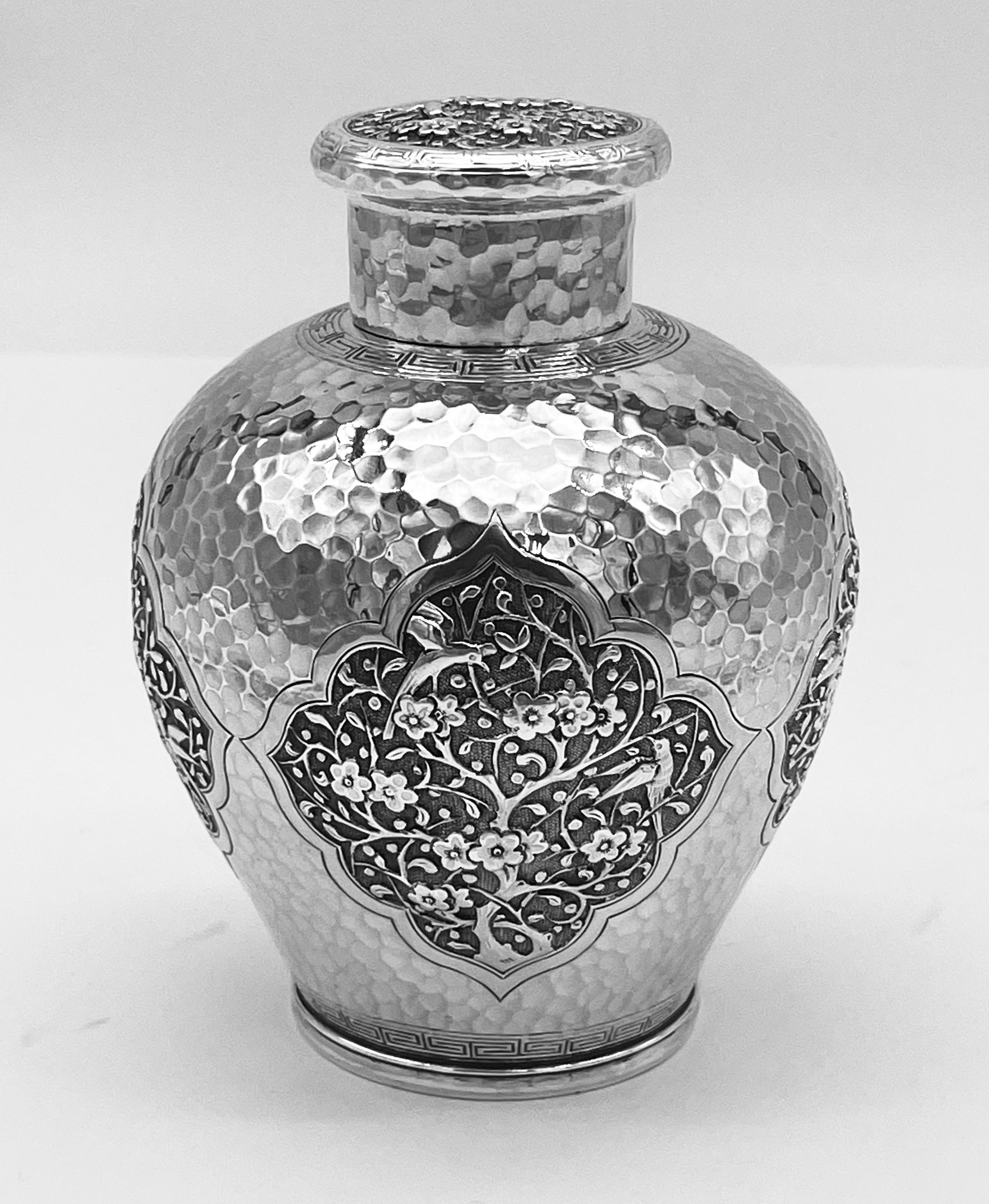 A Chinese Export Silver Tea Caddy embossed and chased with four shaped panels each decorated with prunus and birds, circa 1890. The body has a hammered background and a band of Greek-key decorationa, and the pull-off lid has prunus flowers and two
