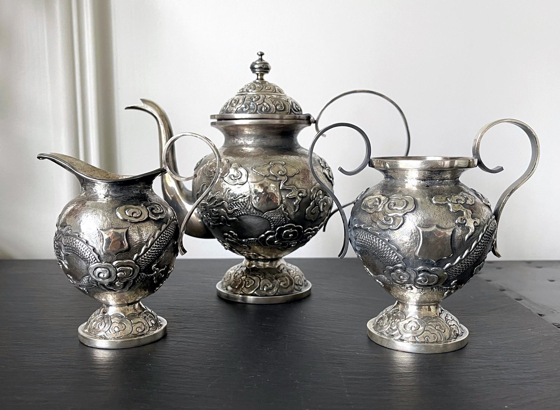 A three-piece set of Chinese export sterling silver tea or coffee service circa early 20th century. The service consists of a lidded tea or coffee pot, a creamer and a sugar bowl. The surface was beautifully decorated with chased high-relief dragons