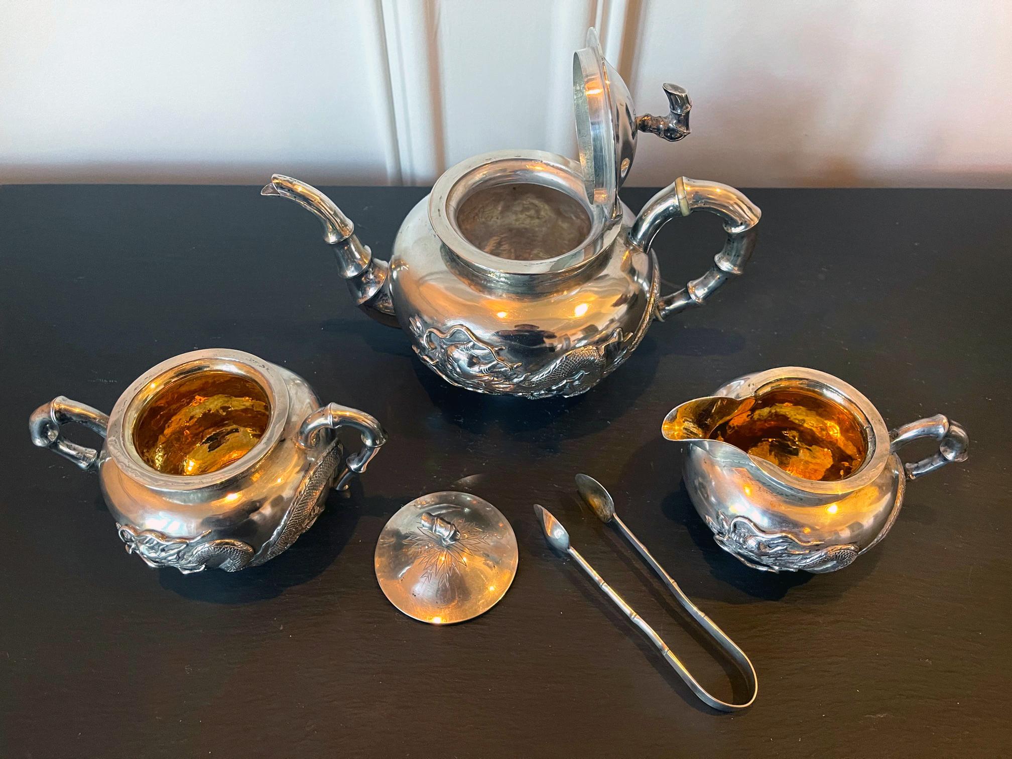 A four piece Chinese export silver tea service set consists of a lidded teapot, a creamer with lid, an open sugar and a tongs. The set was retailed by Zee Wo, a silver retailer located in Shanghai at 121 and 370 Henan Road and operated circa
