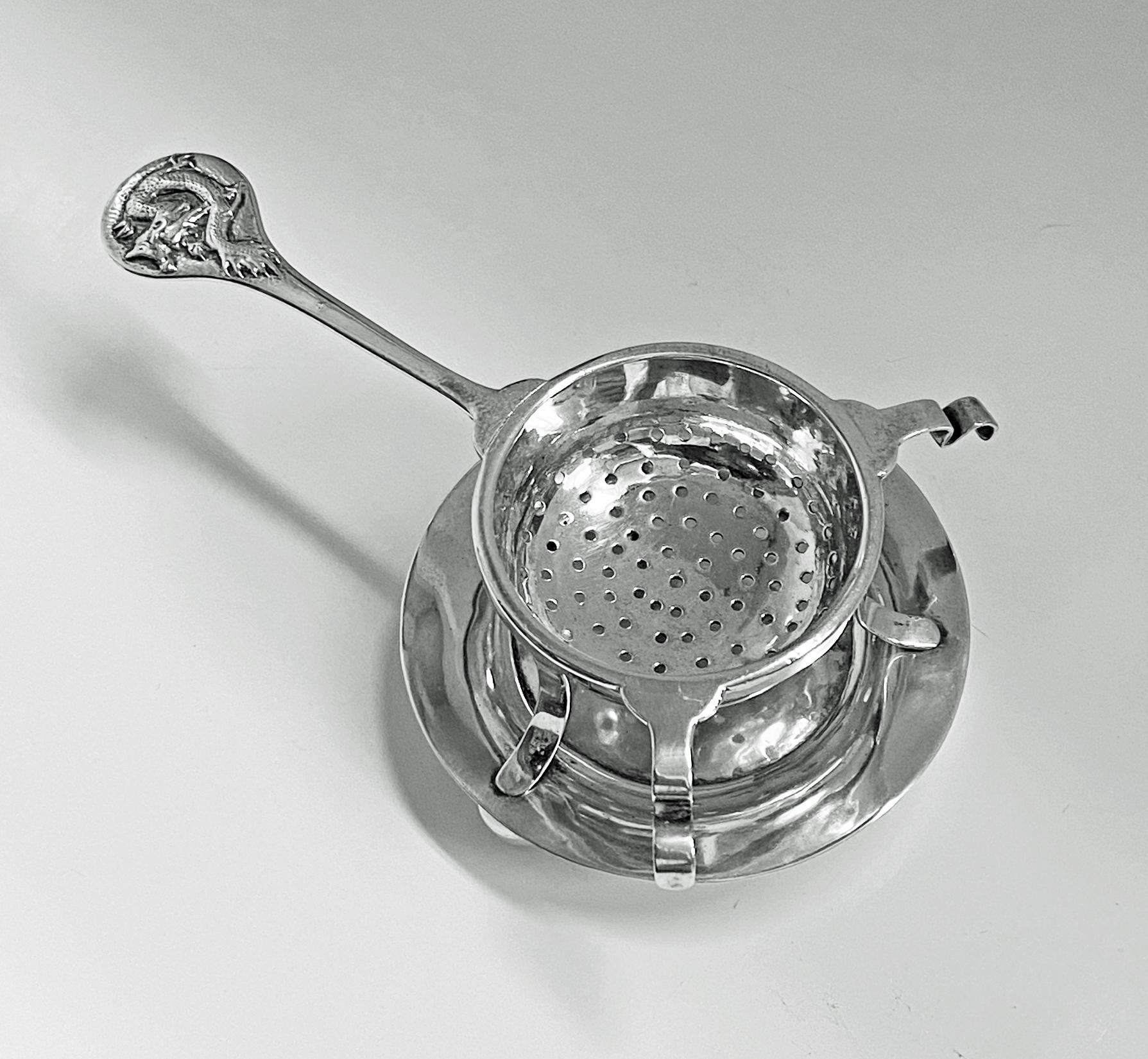 Late 19th century Chinese export silver tea strainer on stand, Tuck Chang, Shanghai, C.1900. Plain design with dragon embellished handle in relief; the bowl pierced, all on plain silver stand with three bun supports. Measures: Length of strainer