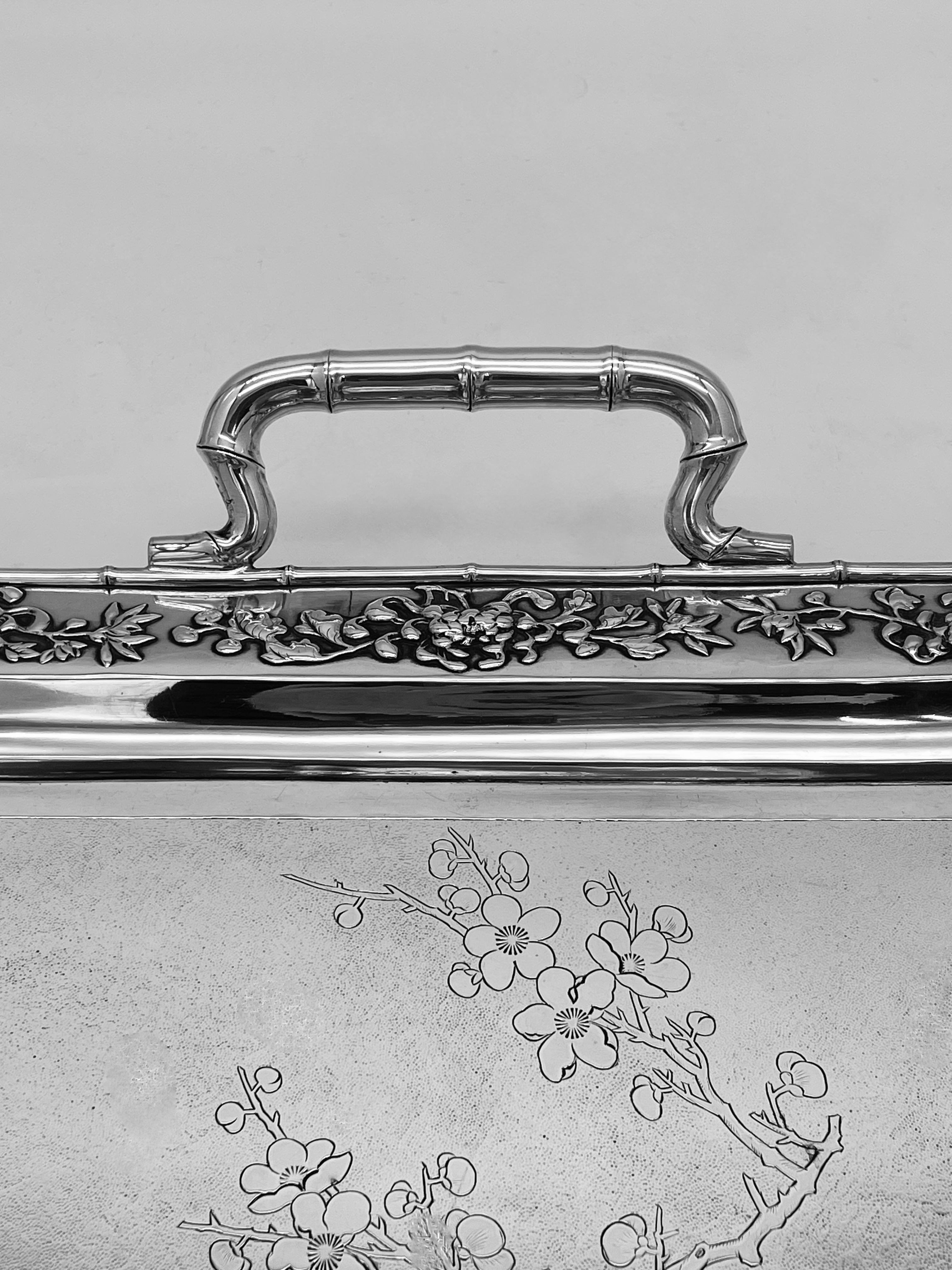 A Chinese Export Silver Tray engraved with prunus on a matte background, with applied chrysanthemum decoration to the border, and with two bamboo shaped handles. The tray was made by '紹記' (Shao Ji) for the retailer Luen Wo in Shanghai, circa 1895.