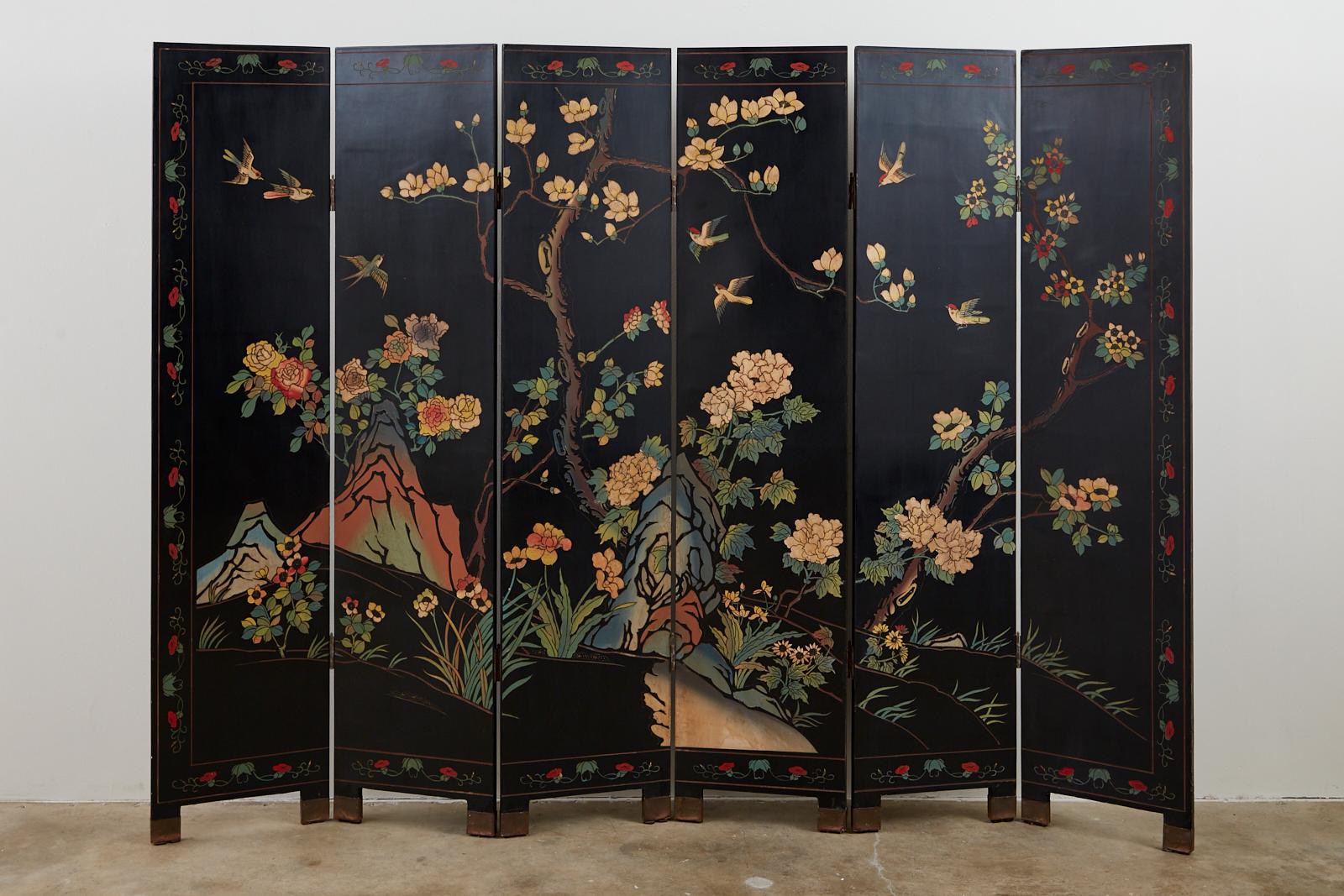 Colorful Chinese export six-panel Coromandel screen. Features a black lacquered ground decorated with a vibrant floral and foliate landscape. The stylized scene has colorful birds and is bordered with a red floral motif. Supported by small