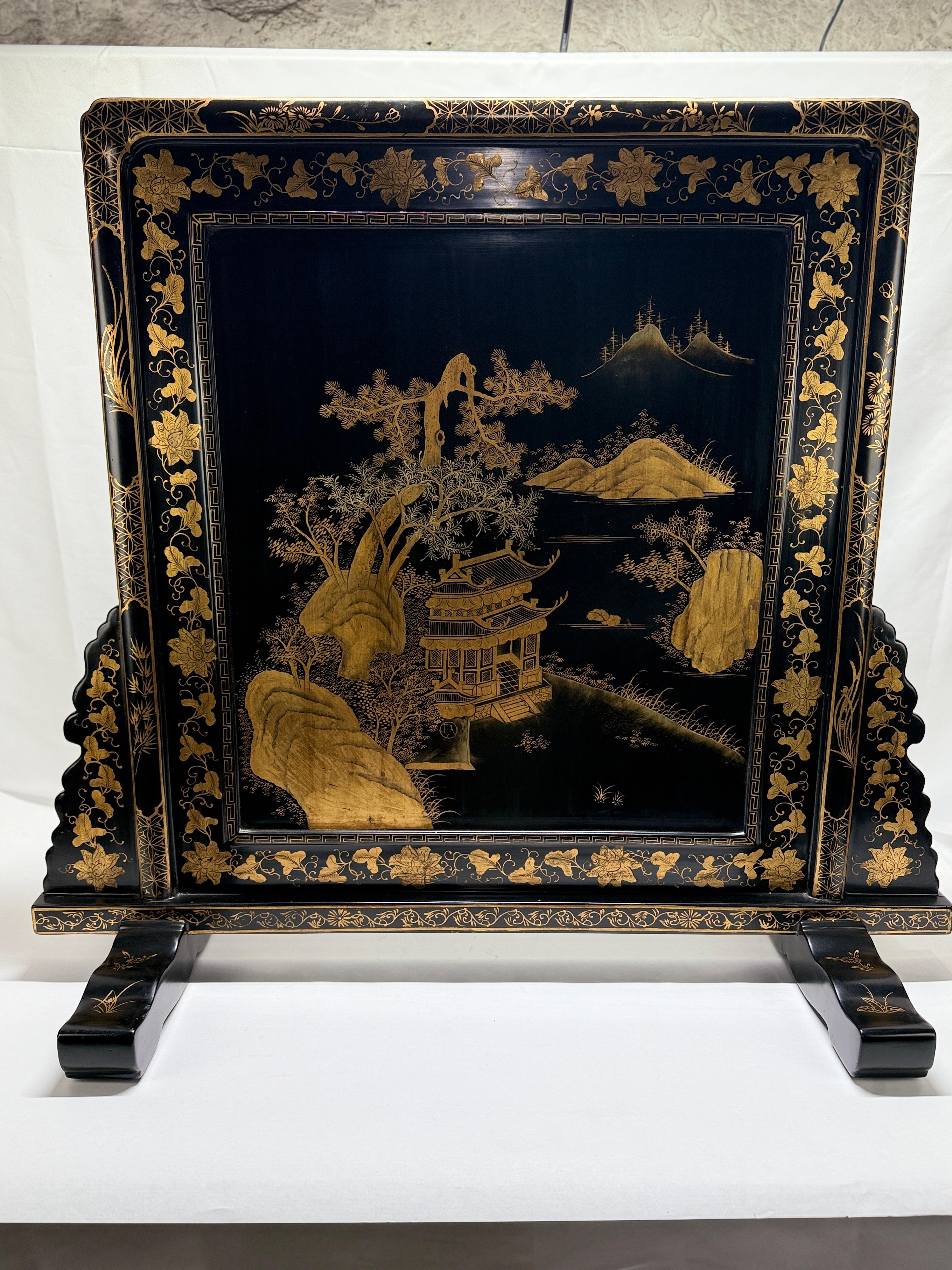 Cet écran de table ou de cheminée laqué de style export chinois illustre le raffinement de l'artisanat chinois, avec une scène complexe peinte en doré sur un fond noir profond. Le panneau est orné d'un paysage finement détaillé représentant un