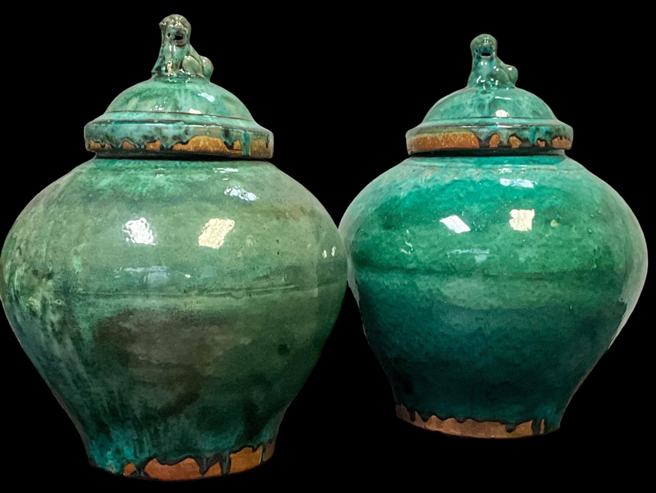 This is a pair of large scale Chinese Export style terracotta green glazed jars. The lids have foo dog finials. Both vessels have a drip majolica glaze with firing irregularities. Highly decorative and unmarked. 