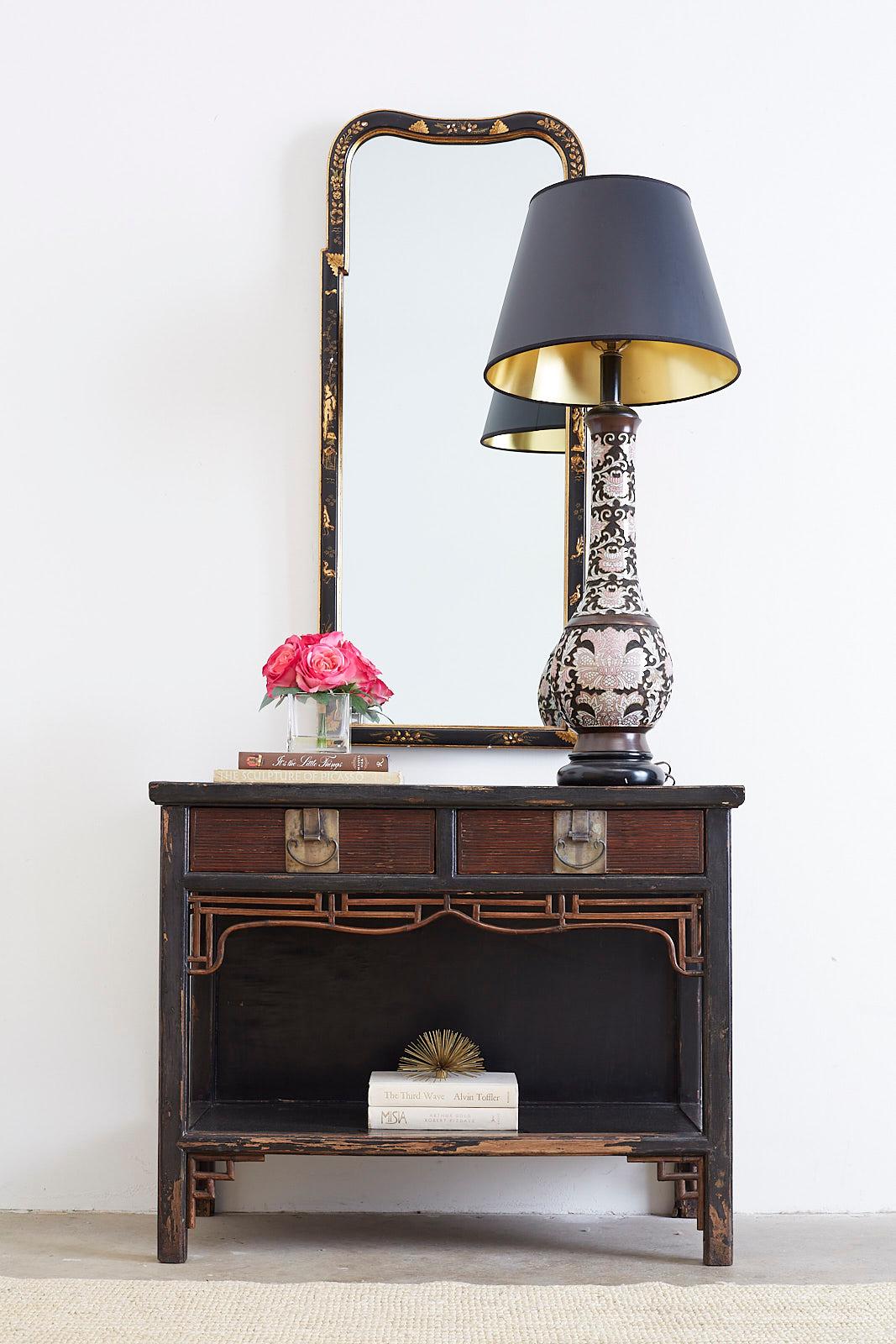 Rustic Chinese export lacquered elm console table featuring an ebonized finish. The table is fronted by two large storage drawers with brass metal pulls. The two tier design is decorated with an open fretwork design of bamboo and rattan. The table