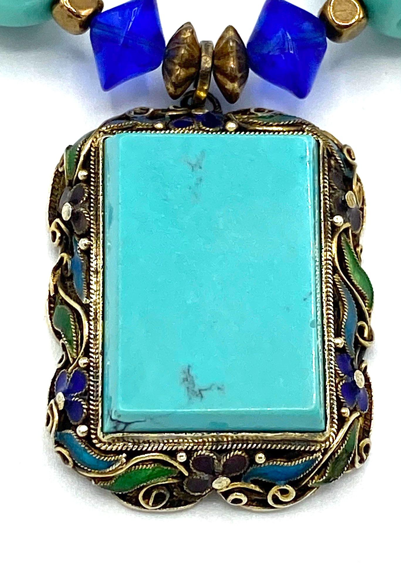A lovely Chinese esport necklace featuring a pendant and clasp of sliver with natural Chinese turquoise. The pendant is gilt silver filigree with green, purple, light and dark blue enamel flowers and accents. Mounted in the center is natural Chinese