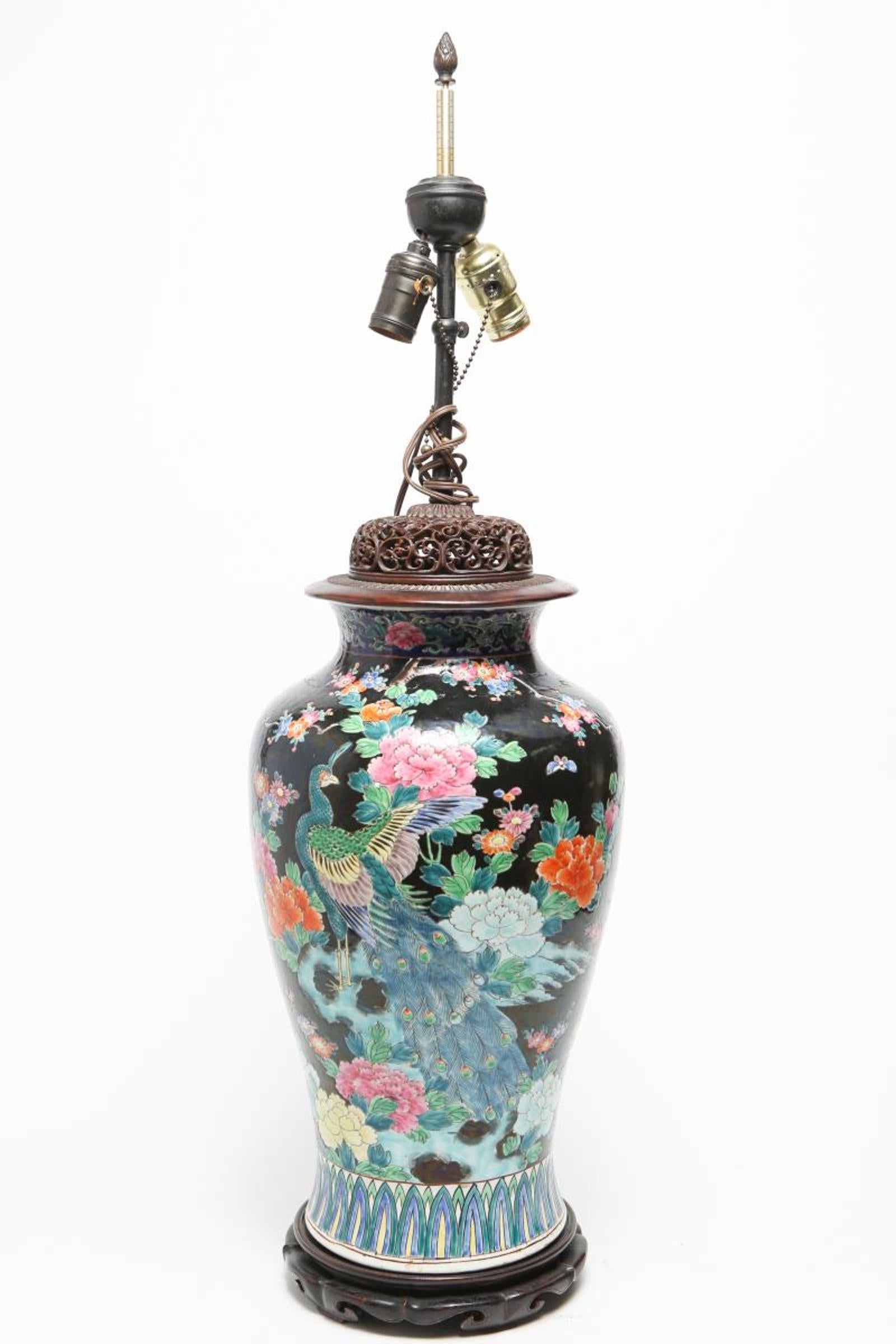 Chinese Famille Noire porcelain balluster jar in floral motif with delicately enameled peonies, camelias, bamboo and phoenix, and a border of stylized stiff feathers, with a carved openwork wood cover. The piece is mounted as a table lamp, on an