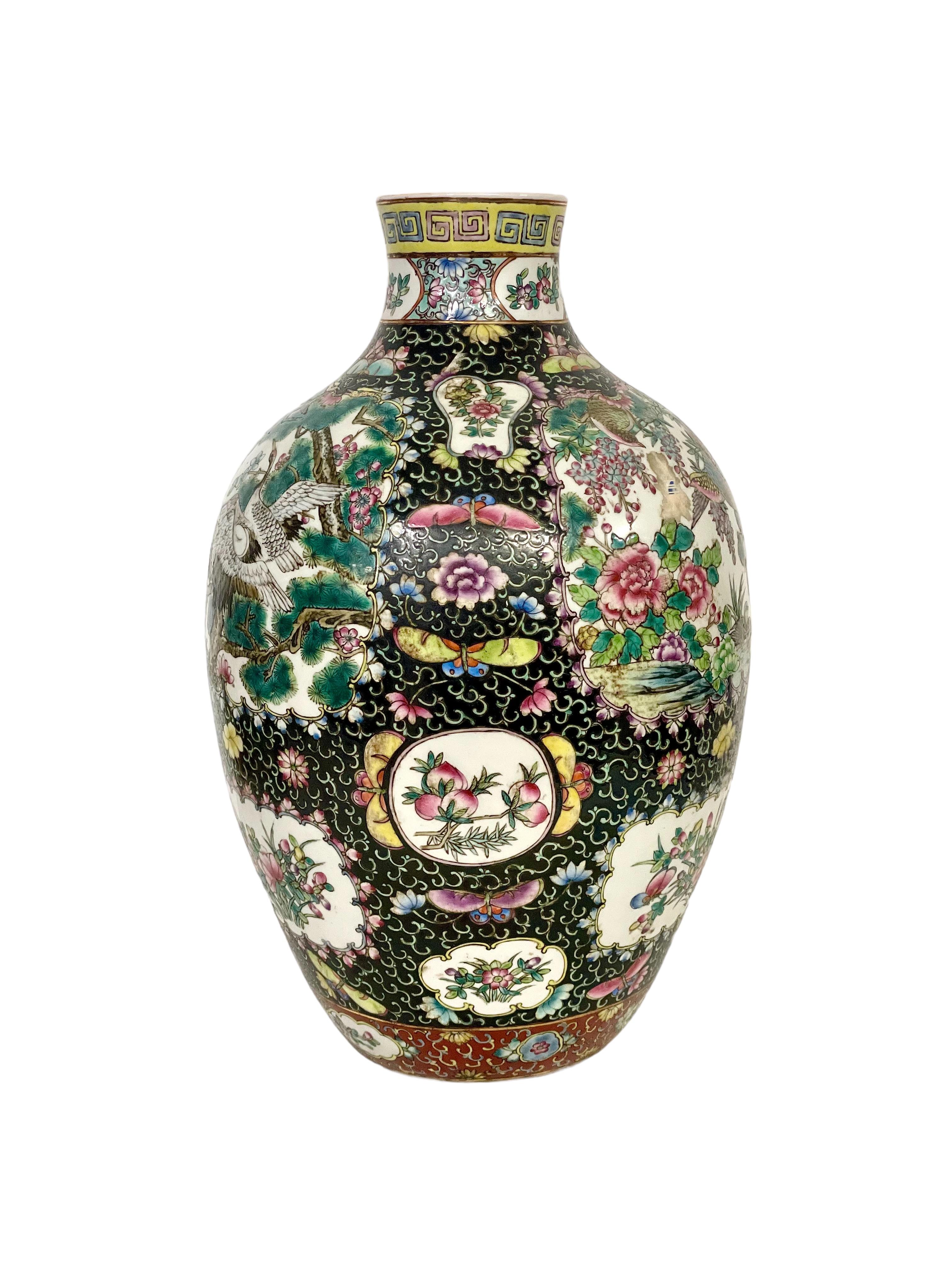 A large and imposing antique Chinese 'Famille Noire' porcelain vase, intricately decorated all over with vibrantly coloured butterflies, blossoms and birds, including a crane and a phoenix. Its narrow rim is highlighted with a band of bright yellow,
