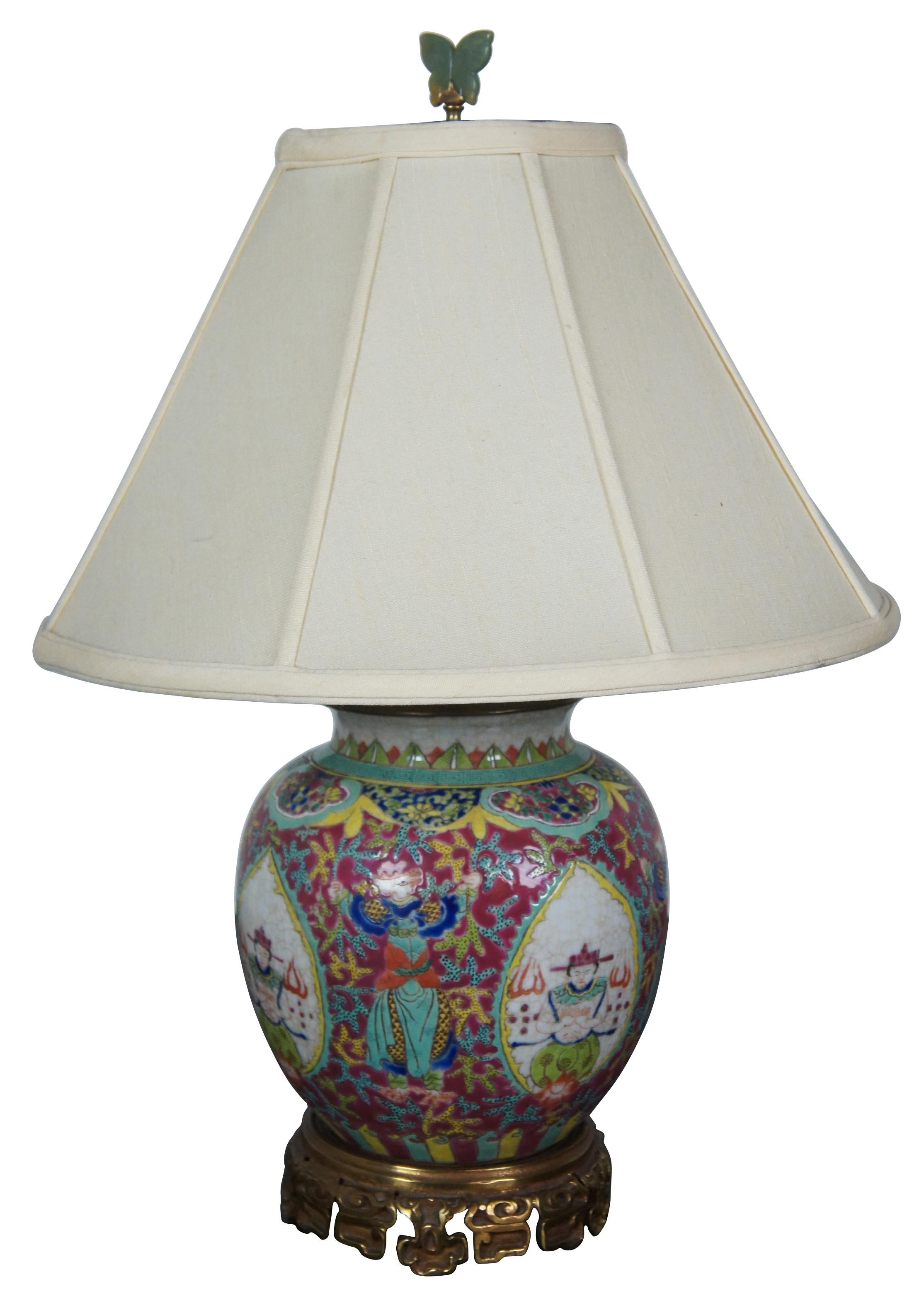 Vintage footed bronze and porcelain ginger jar table lamp featuring enameled figures with tongues of fire alternating with a dancing figure with the head of a chicken or bird. Features a jade butterfly finial and Greek key border.

Measures: Shade