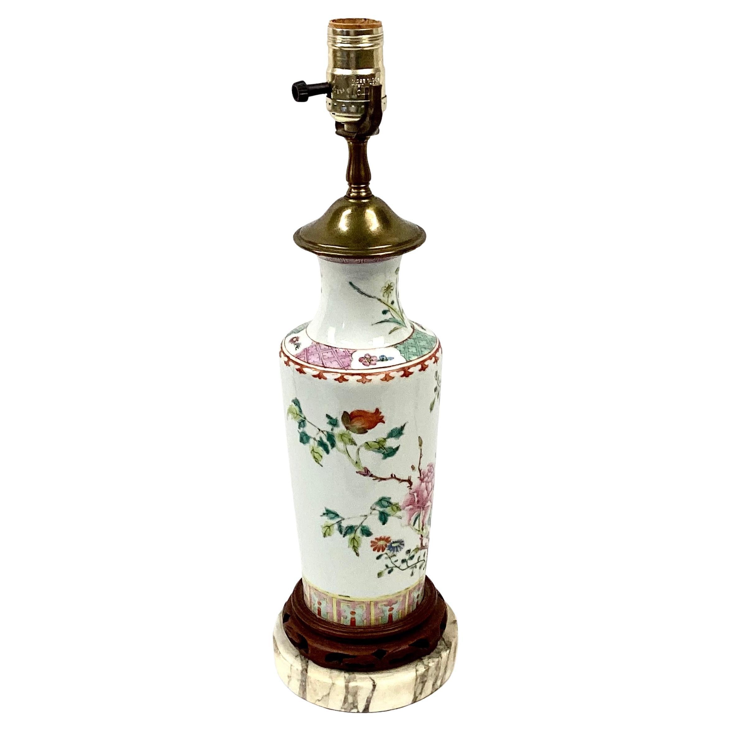 19th century Chinese famille rose floral and bird porcelain lamp. Pink, green and teal colors on a white background. Lamp sits on a carved wooden and marble base. In good working condition.