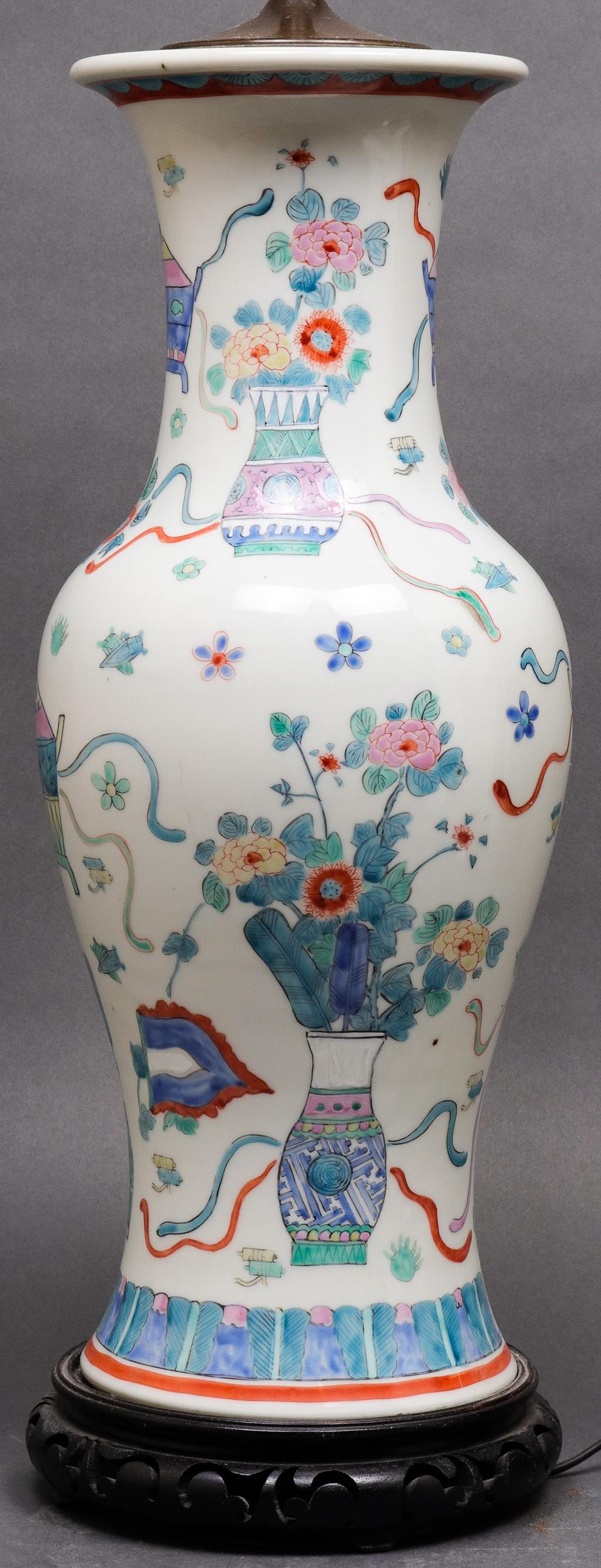 Chinese famille rose porcelain vase mounted as a table lamp, with hand painted vase and censor decoration, mounted on openwork wood carved base, brass finial. Measures: 34