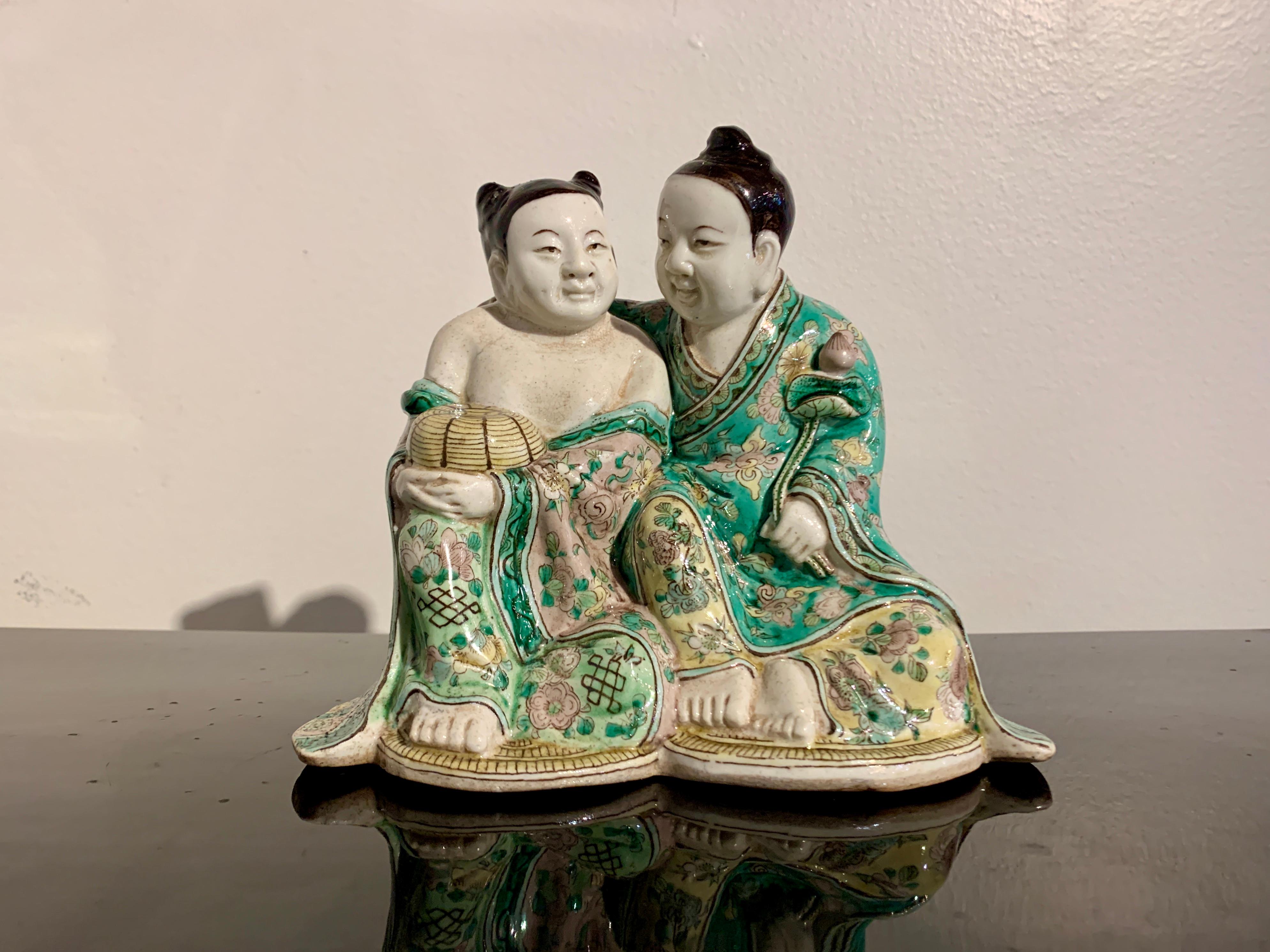 A delightful famille verte enameled porcelain figural group of the He-He Er Xian, the Twins of Harmony and Union, late Qing Dynasty, circa 1900, China.

The He-He Er Xian are portrayed as a pair of smiling, corpulent youths huddled together. They