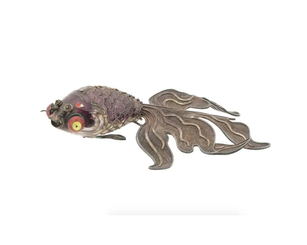 An antique Chinese articulated fish pendant crafted of silver with a wire forming details throughout the tail fin, scales, dorsal fin, hanging fins at the underside. The body is covered with a purple enamel, mouth and eyes are covered with red and
