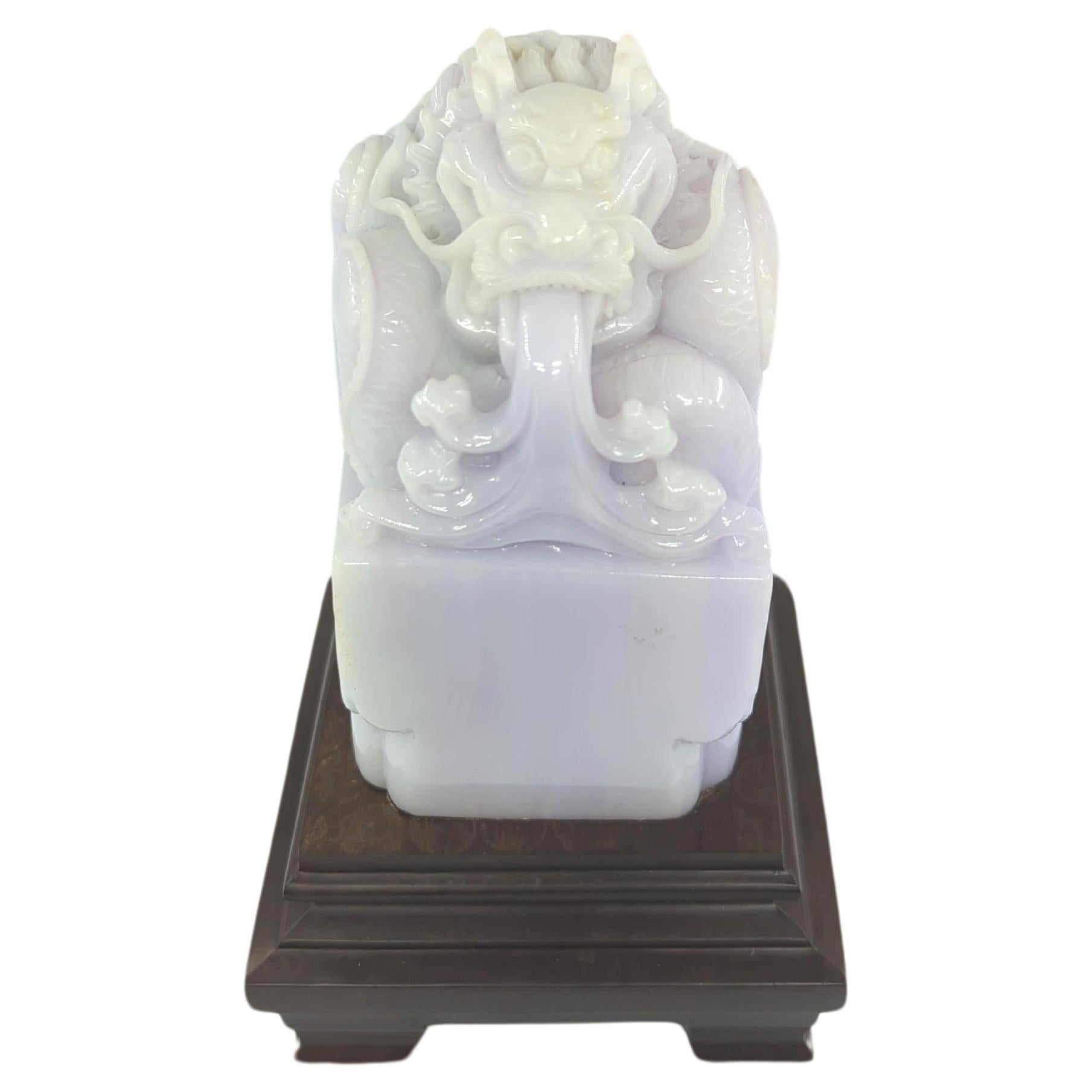 This large exquisite A-grade jadeite seal presents a masterful carving of a scaly dragon, rendered in a delicate shade of pale lavender. 

The dragon, a symbol of power, strength, and good luck, is intricately carved atop a square boulder, adding a