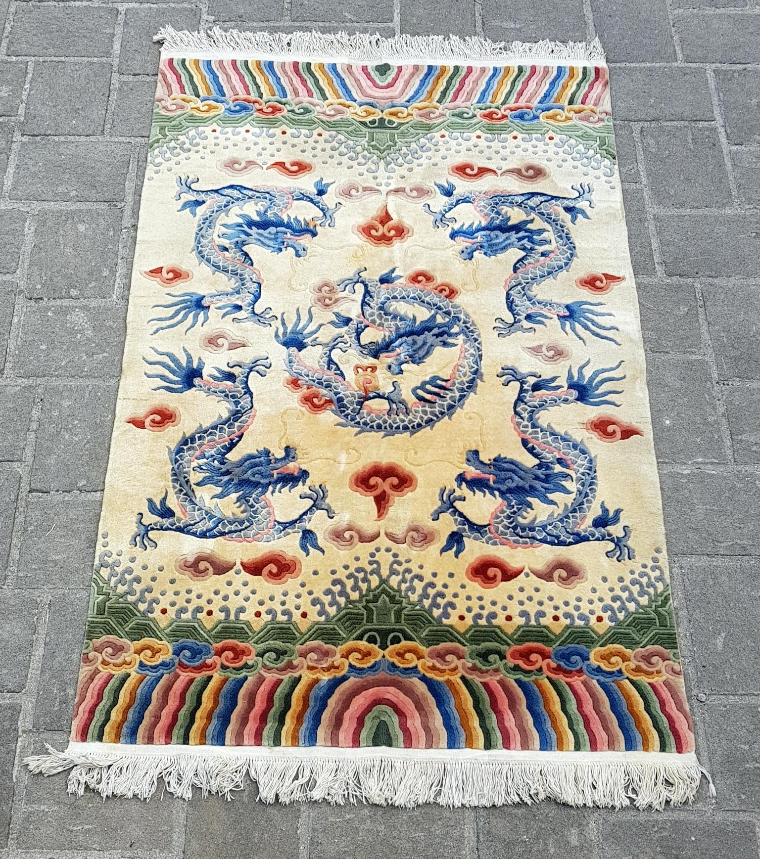 This colorful and vibrant Chinese rug depicts five dragons in blue against an ivory colored base surrounded by clouds in red, pink and purple colors.
At the centre of this piece is a powerful dragon playing with the burning pearl, surrounded by