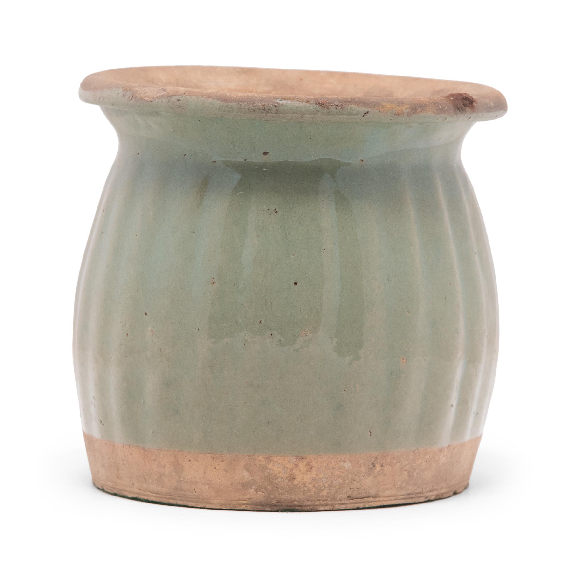 Dated to the early 20th century, this glazed ceramic jar features a flared lip and bulbous sides textured by a pattern of ridges. A celadon-green glaze coats the swelling sides, gently aged with minor crazing and pitted wear. The top opening is wide