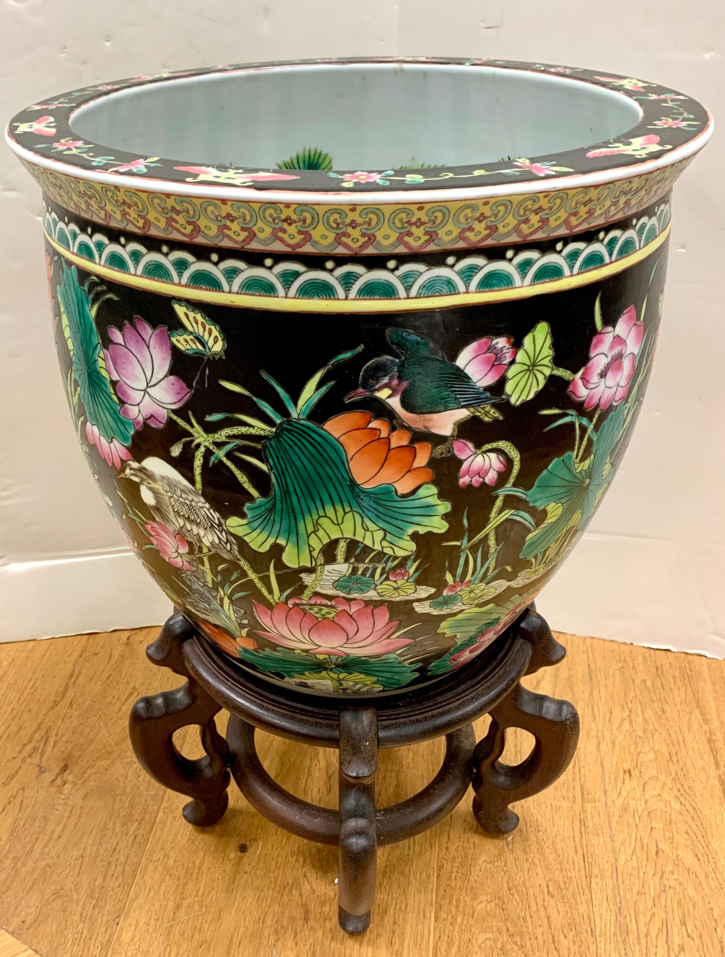 Beautiful Chinese porcelain planter painted with colorful florals and greenery on a black ground on the exterior. Interior has painted fish amidst seaweed. The fishbowl sits atop a carved wooden pedestal.
Fishbowl 16” W x 14.5” H.